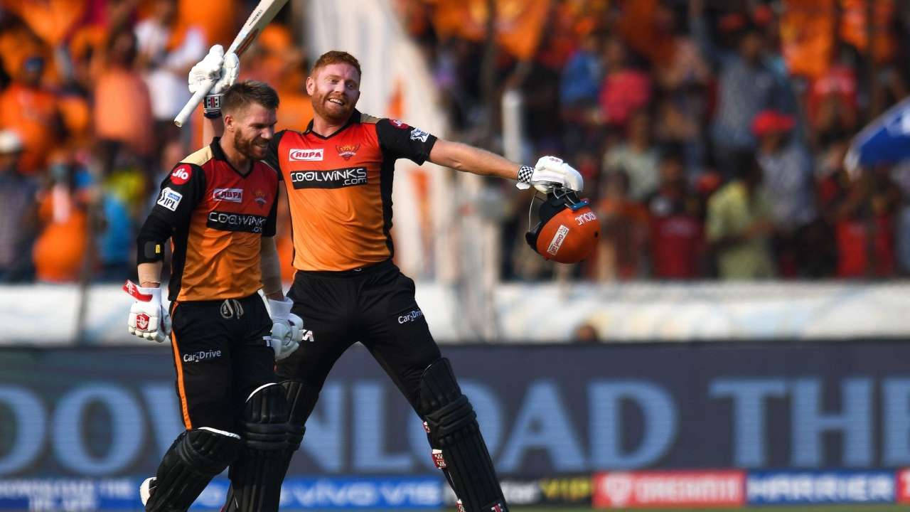 Sunrisers Hyderabad 桌布 壁紙 — 兩名身穿橙色球衣的板球運動員在模糊的人群背景下舉起球棒和頭盔慶祝勝利。