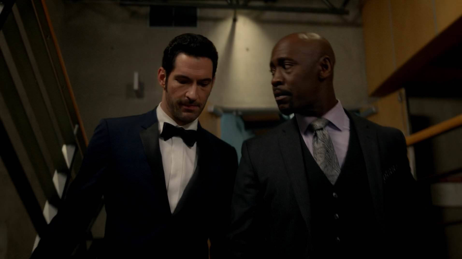 路西法 桌布 壁紙 — 兩名身穿正式西裝的男子在昏暗的工業環境中，在聚焦的頂燈照明下走下樓梯。