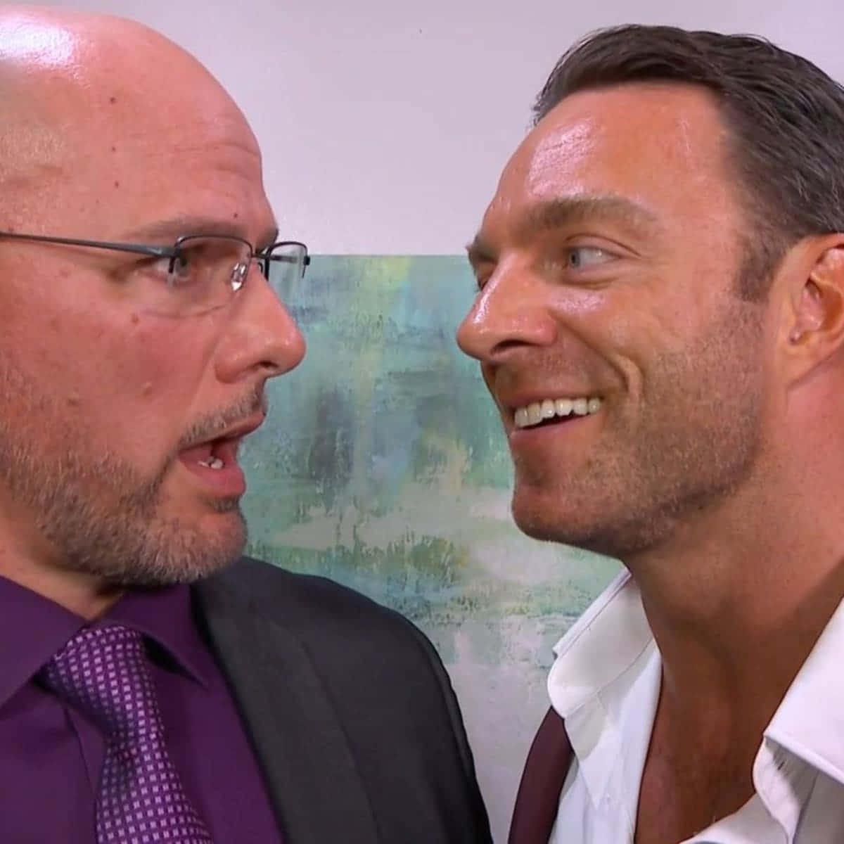 WWE 桌布 壁紙 — 兩名身穿正裝的男子在柔和抽象牆壁背景前，帶著富有表現力的笑容面對面。