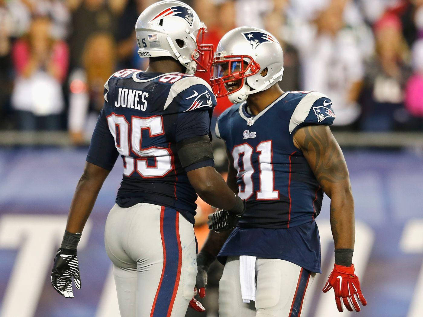 New England Patriots 桌布 壁紙 — 兩名身穿海軍藍球衣的新英格蘭愛國者隊美式足球員在球場燈光下於比賽中慶祝。
