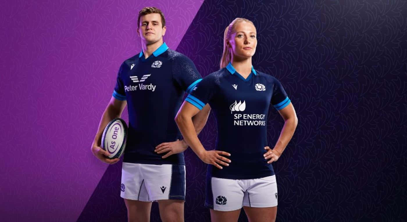 Scotland Rugby 桌布 壁紙 — 兩名身穿海軍藍球衣的橄欖球運動員在紫色圖案背景前自信地擺姿勢，其中一人手持橄欖球。