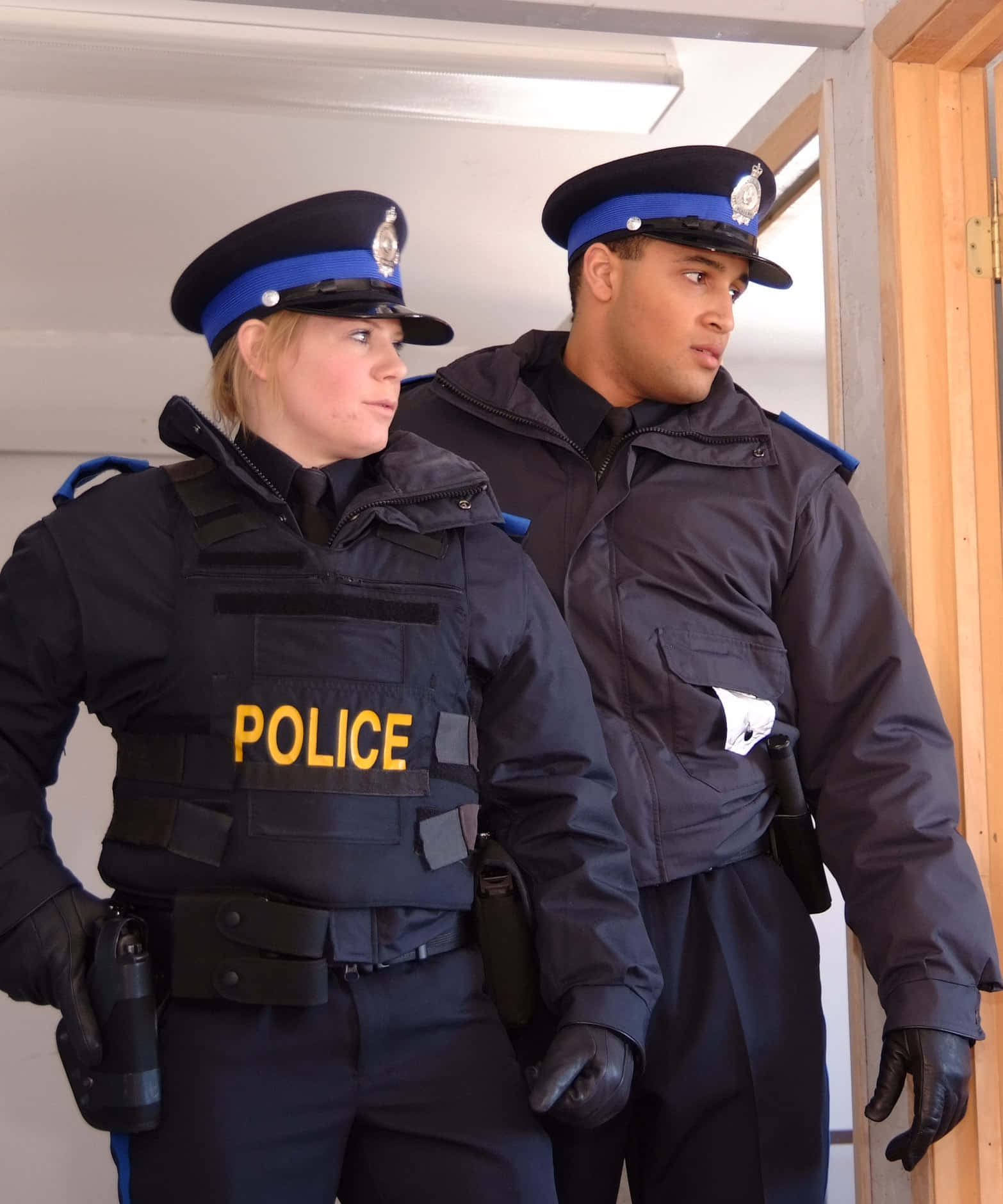警察 桌布 壁紙 — 兩名身穿深色制服的警察在室內警覺地站著，表情嚴肅。