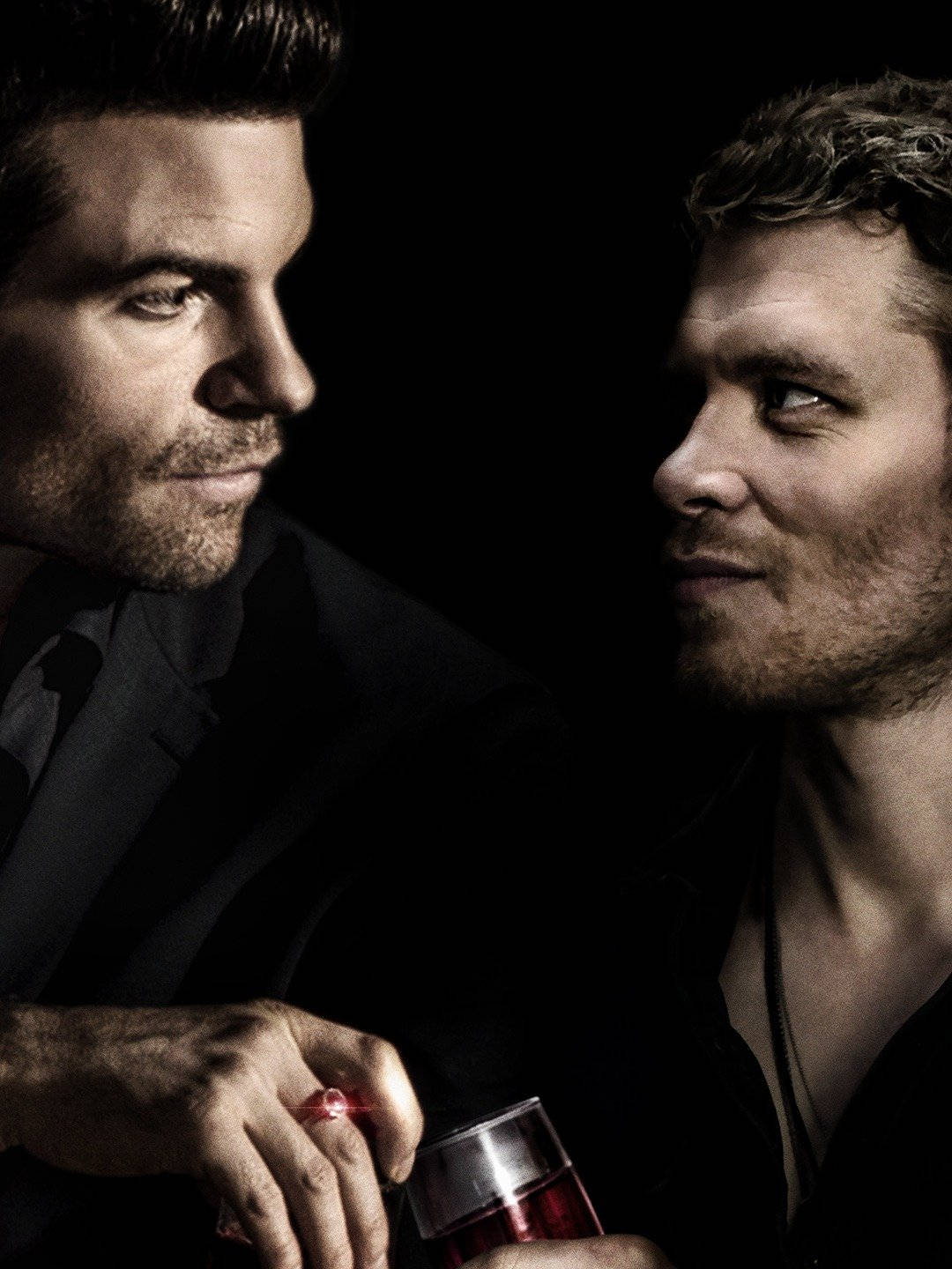 elijah mikaelson 桌布 壁紙 — 兩名身穿深色西裝的男子在昏暗的環境中面對面，其中一人手持一杯紅色液體。