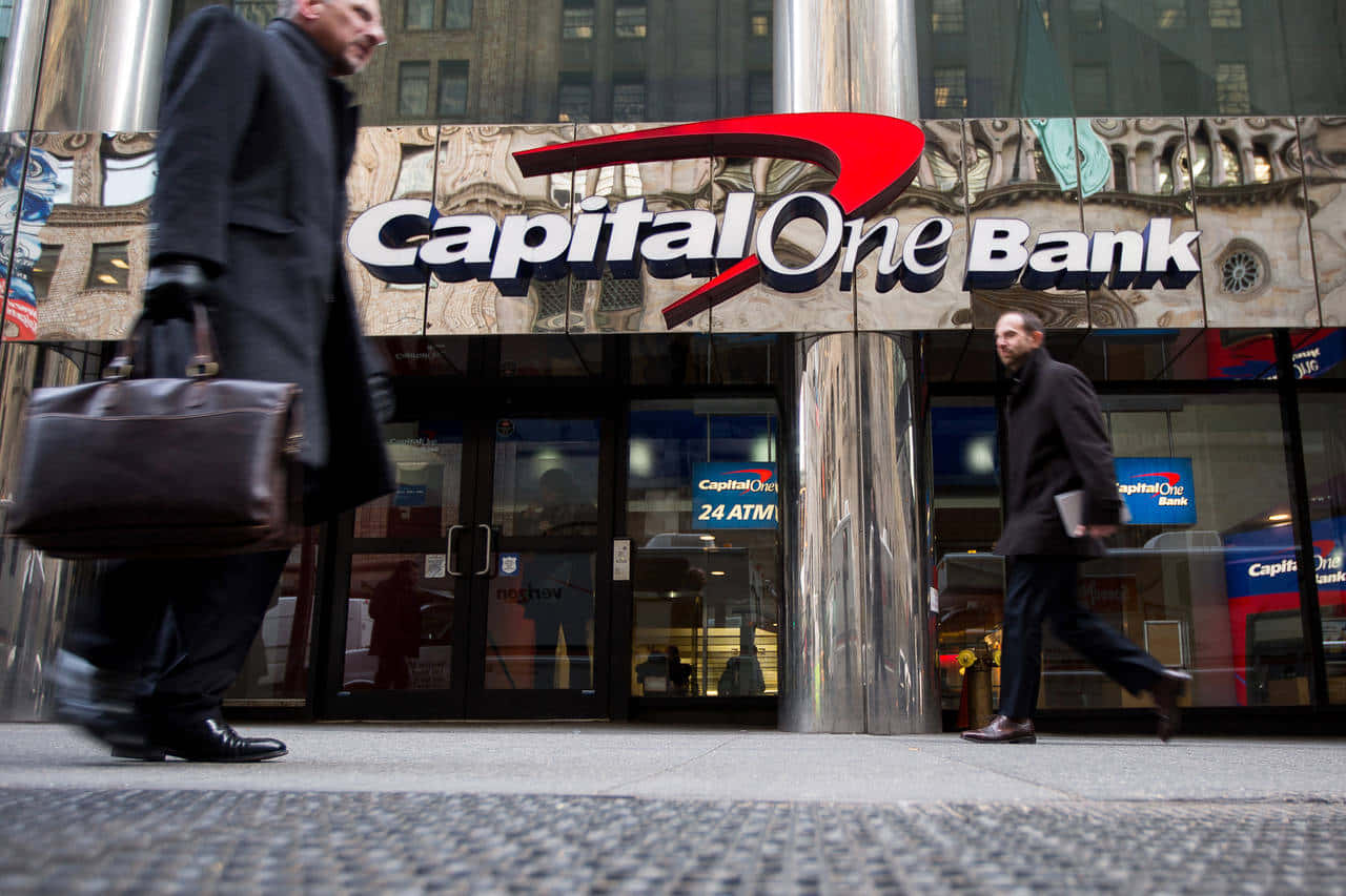 人物 桌布 壁紙 — 兩名身穿深色西裝的男子走過一間Capital One銀行，該銀行設有反光玻璃外牆和24小時自動櫃員機標誌。