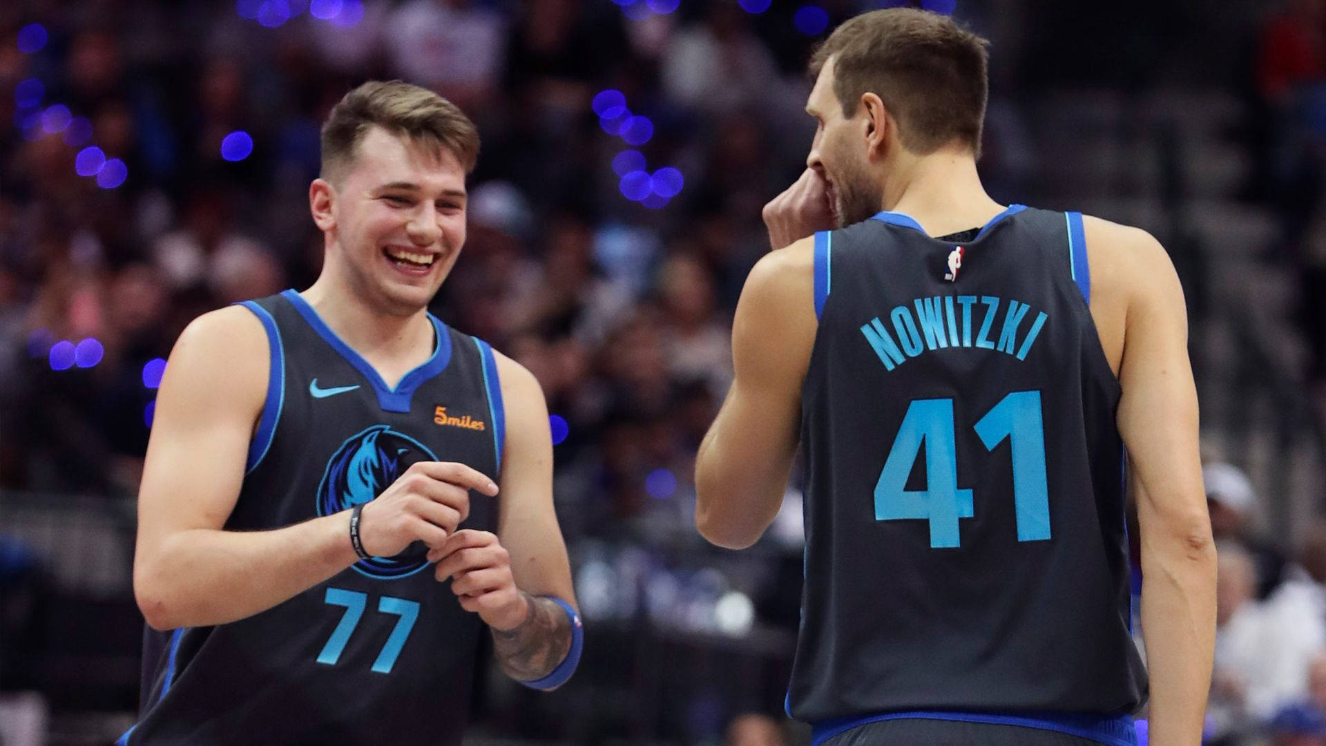 Luka 桌布 壁紙 — 兩名身穿深藍色球衣的籃球運動員在燈光明亮的球場上分享歡樂時刻，背景是模糊的觀眾。