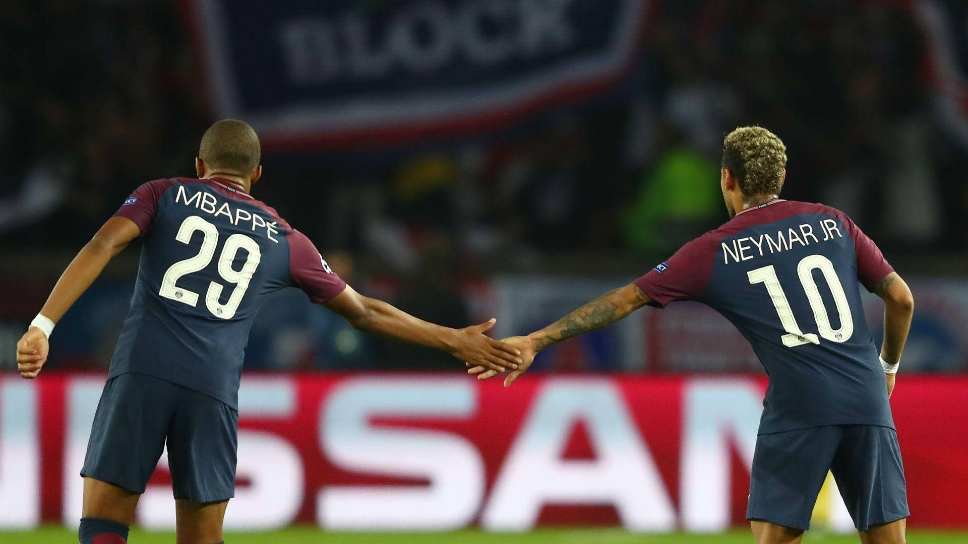 Kylian Mbappe 桌布 壁紙 — 兩名身穿深藍色球衣的足球運動員在夜間燈火通明的球場上握手。