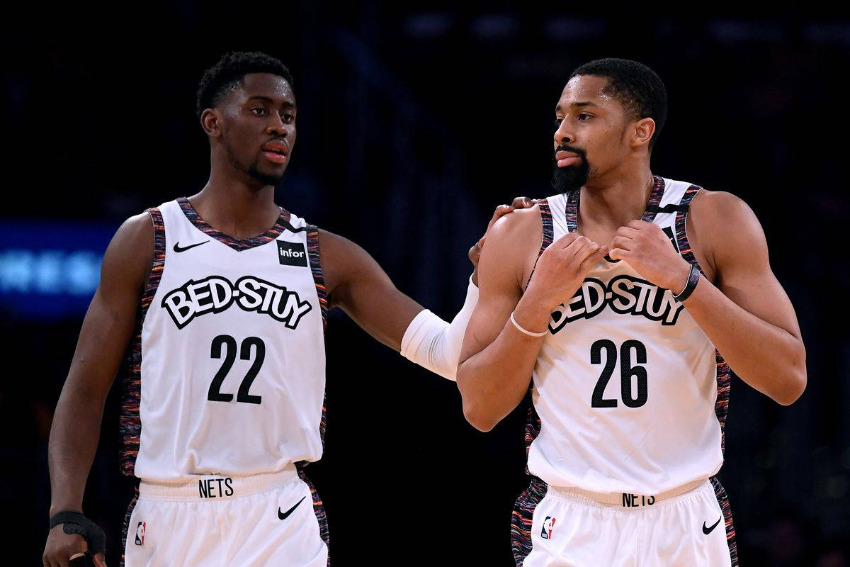 caris levert 桌布 壁紙 — 兩名身穿白色Bed-Stuy Nets球衣的籃球運動員在球場上緊密站立，一人手臂搭在另一人肩上，兩人專注地向前看。