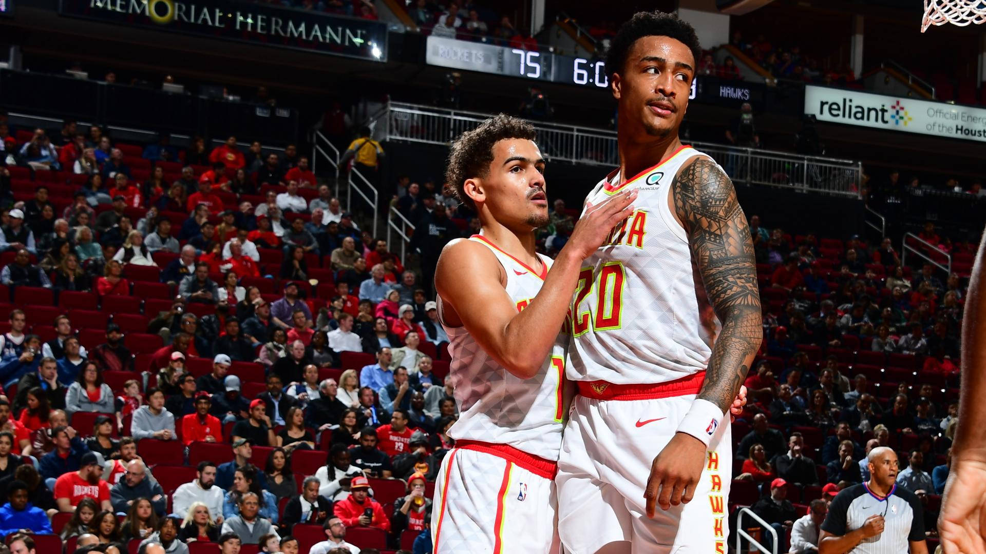 John Collins 桌布 壁紙 — 兩名身穿白色Hawks球衣的籃球運動員在燈光明亮的球場上擁抱，身後是座無虛席的紅色體育館。