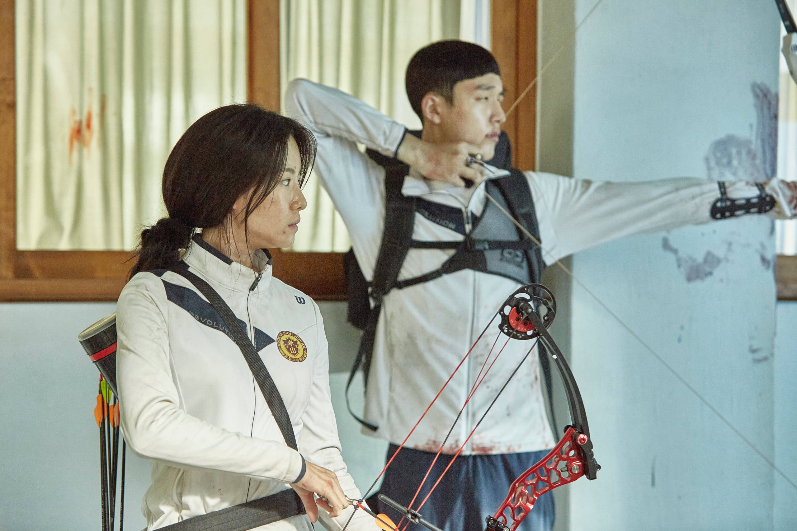 Archery 桌布 壁紙 — 兩名身穿白色制服的弓箭手在室內專注地瞄準，一個拉緊紅色弓，另一個準備好她的弓。
