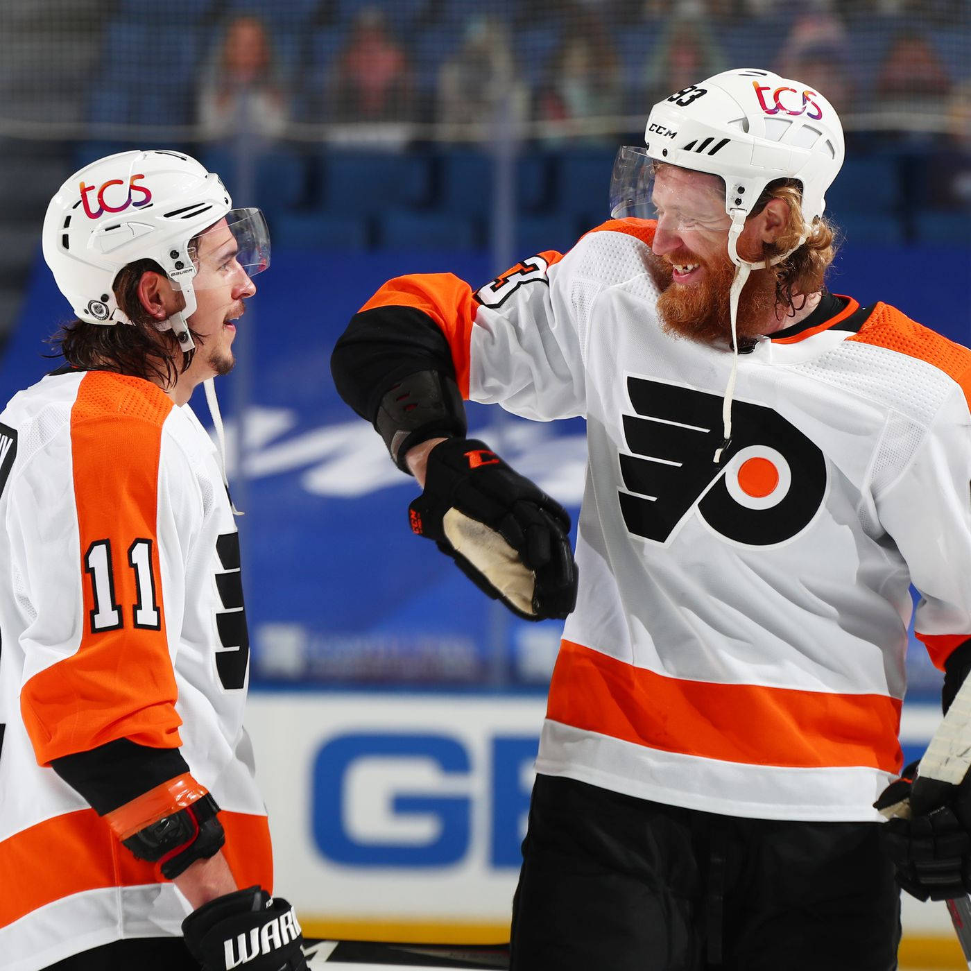 hockey 桌布 壁紙 — 兩名身穿白色和橙色球衣的費城飛人冰球球員在比賽期間在冰上分享歡樂時刻。