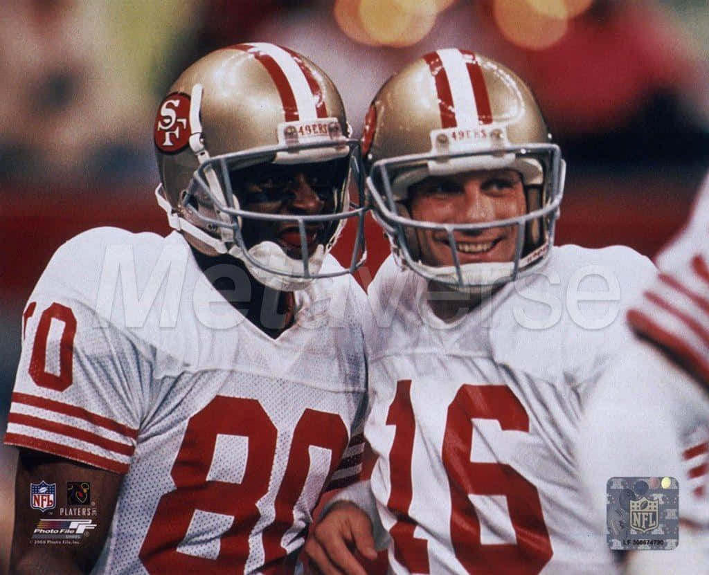 Joe Montana 桌布 壁紙 — 兩名身穿白色和紅色球衣的舊金山49人美式足球員在球場上微笑熱情擁抱。