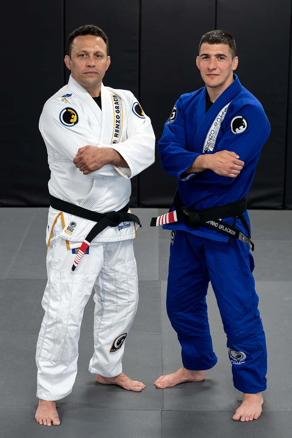 martial arts 桌布 壁紙 — 兩名身穿白色和藍色柔道服的男性柔道選手，自信地交叉雙臂站在灰色墊子上，背景是黑色牆壁。