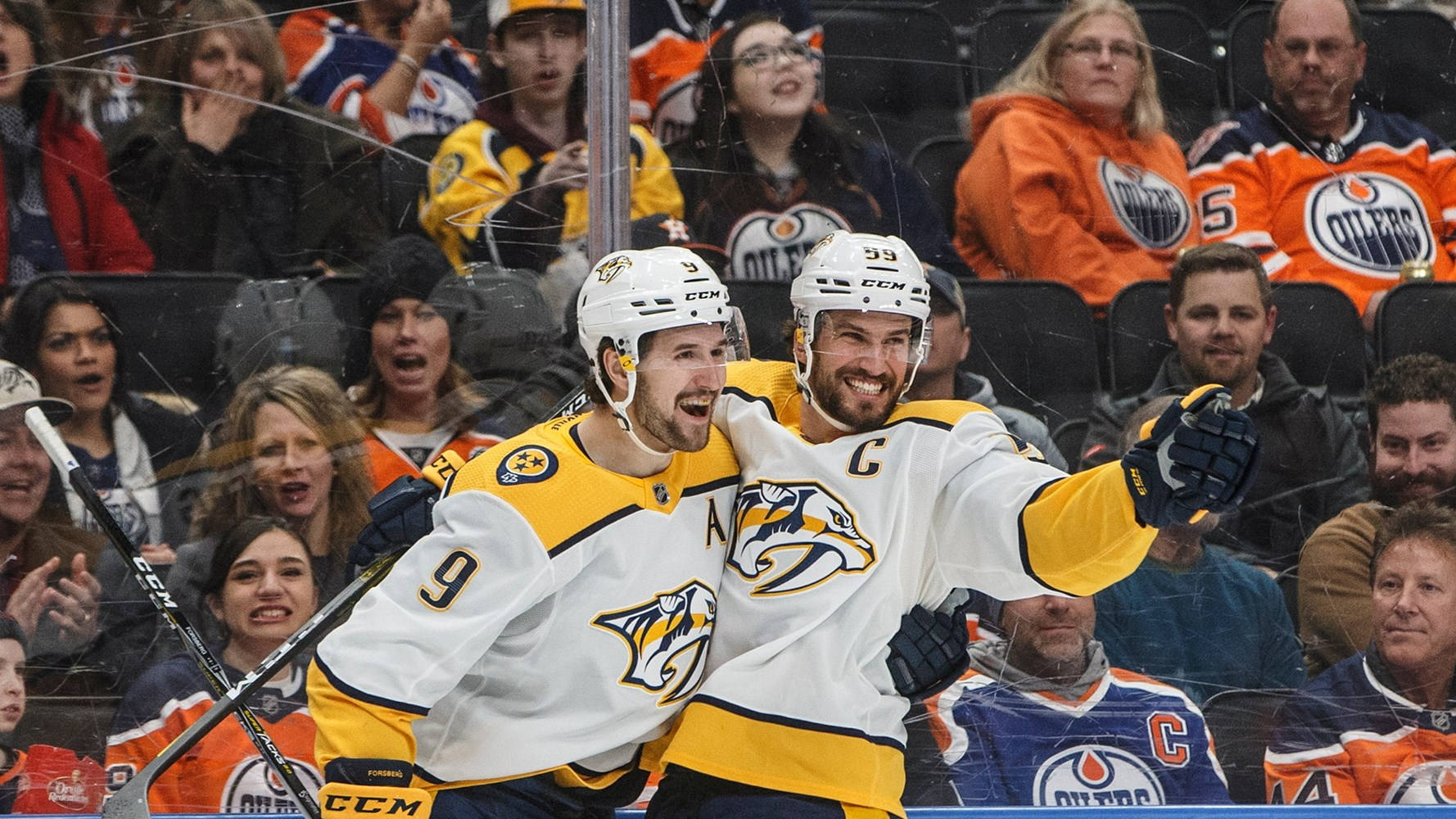 Nashville Predators 桌布 壁紙 — 兩名身穿白色和黃色球衣的冰球運動員在背景歡呼的球迷面前慶祝進球。