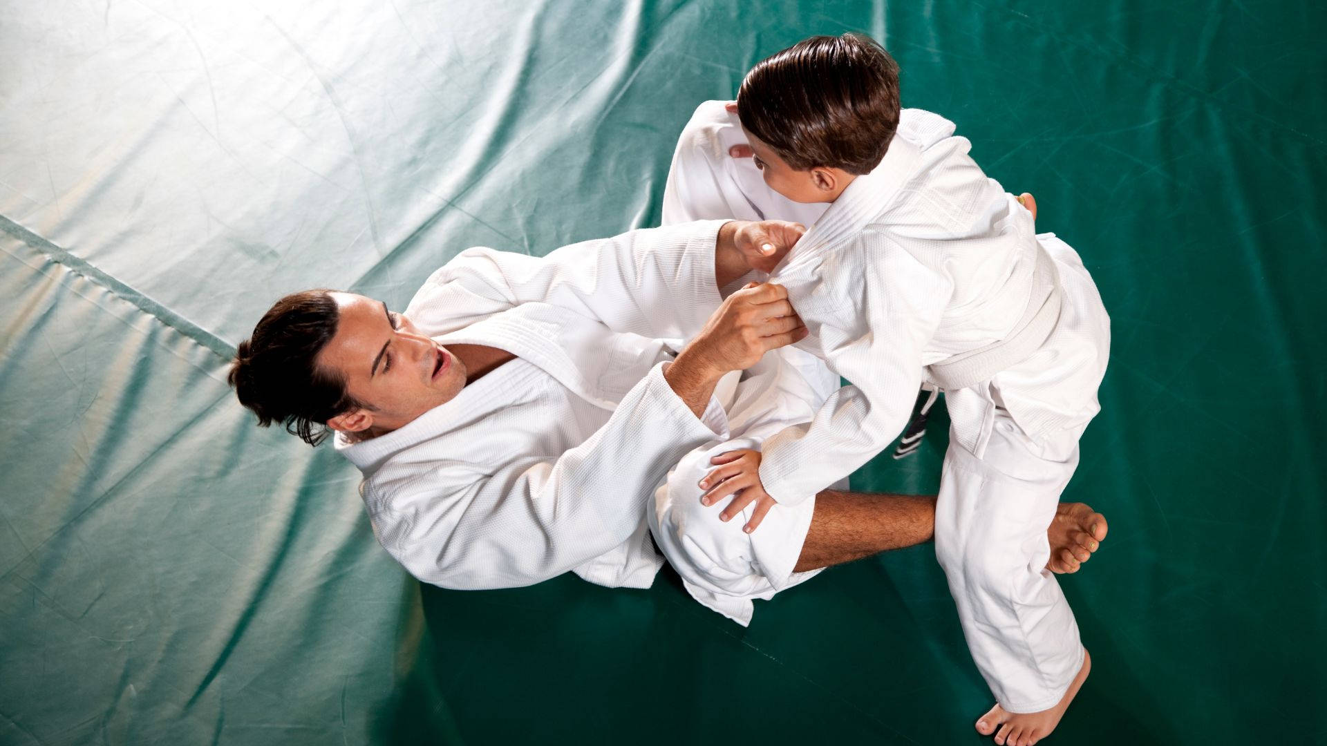 martial arts 桌布 壁紙 — 兩名身穿白色柔道服的武術家從俯視角度在綠色軟墊上激烈纏鬥。