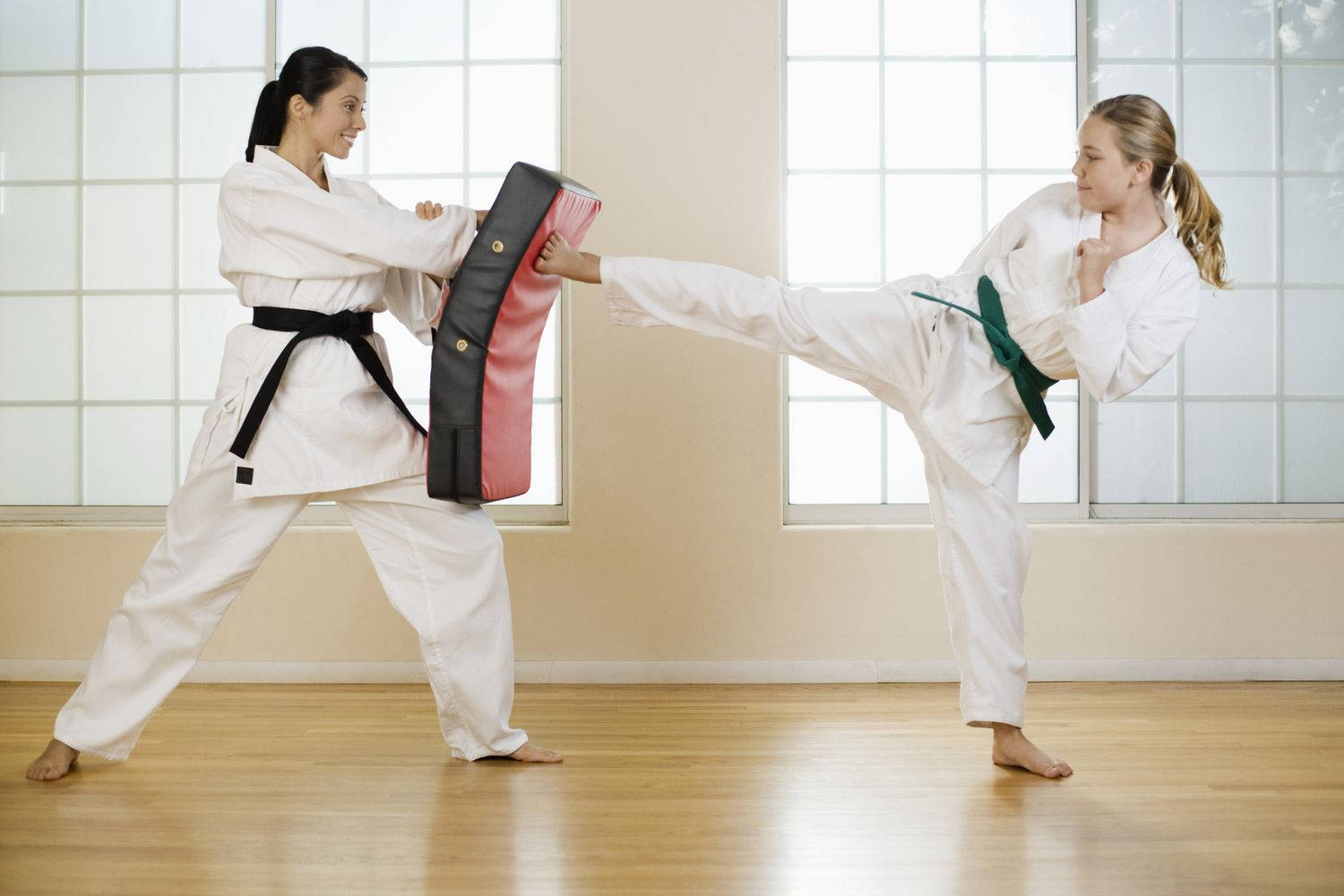 Athletic 桌布 壁紙 — 兩名身穿白色武術制服的女性在室內訓練，其中一人踢著另一人拿著的紅黑色靶。