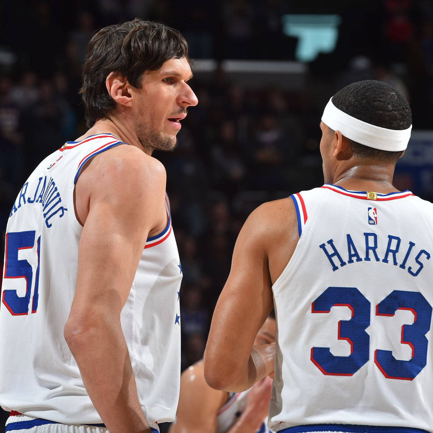 NBA 桌布 壁紙 — 兩名身穿白色球衣、帶有藍紅飾邊的籃球運動員在明亮的場館燈光下，於比賽中激烈對峙。