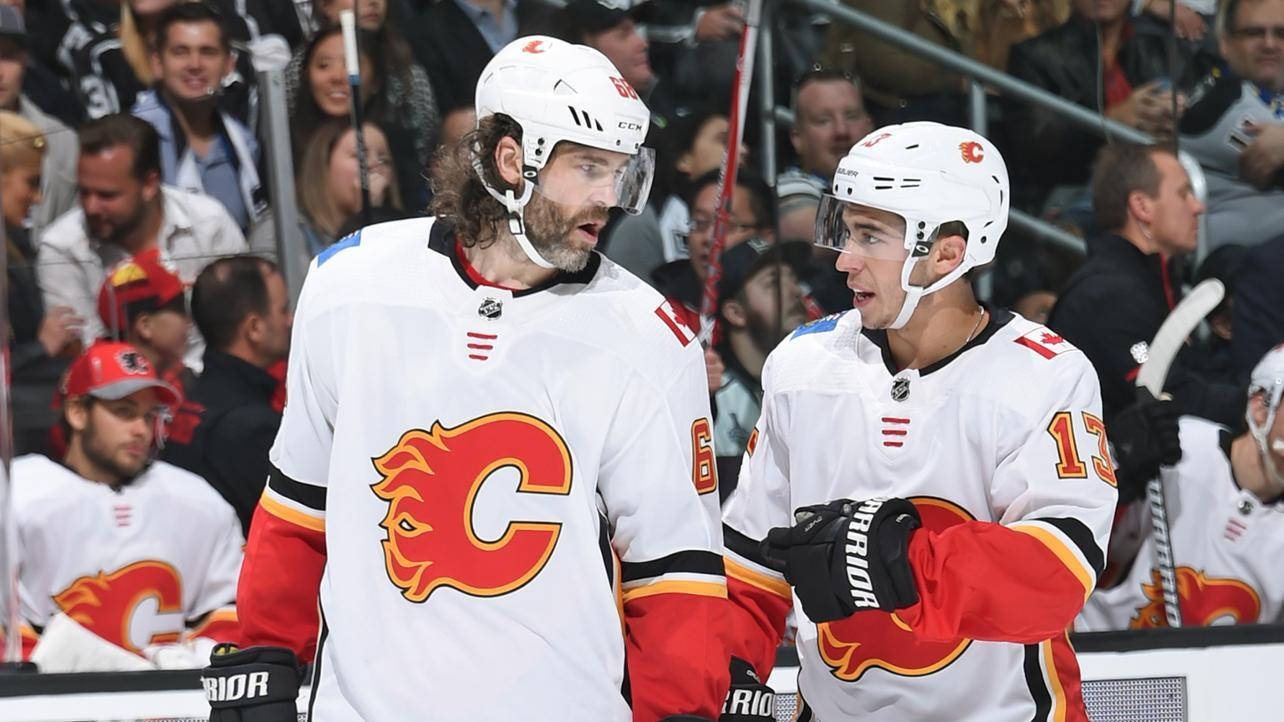 Johnny Gaudreau 桌布 壁紙 — 兩名身穿白色球衣的卡加利火焰隊冰球球員在冰場附近熱烈交談，背景有球迷。
