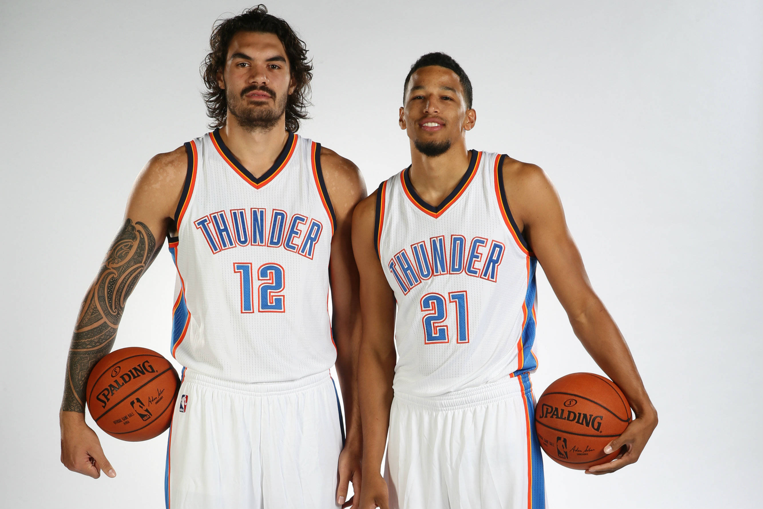史蒂芬·亞當斯 桌布 壁紙 — 兩名身穿白色球衣的奧克拉荷馬城雷霆籃球運動員在純白色背景前自信地手持Spalding籃球擺姿勢。