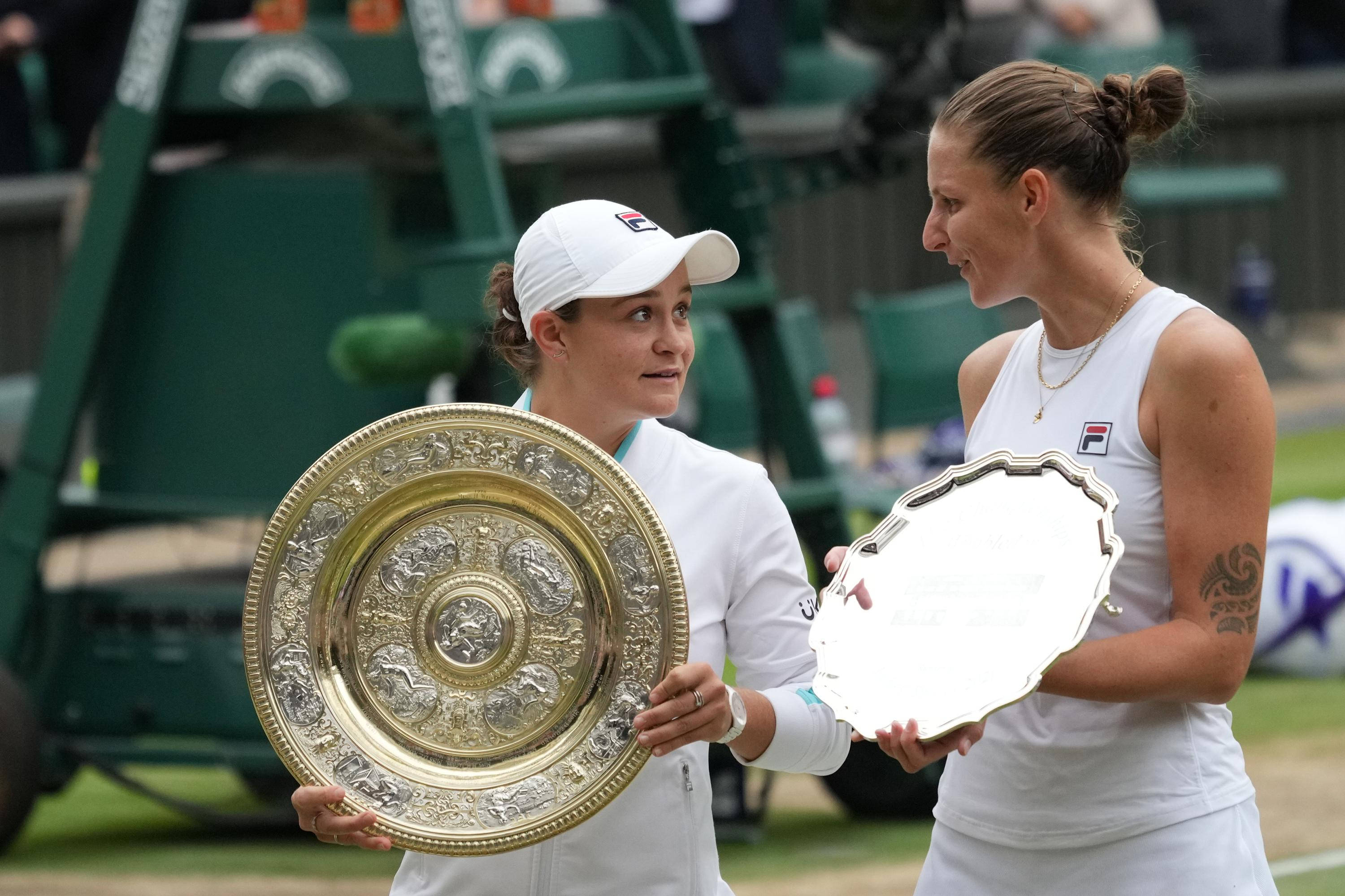 Trophy 桌布 壁紙 — 兩名身穿白色球衣的女網球選手在草地上手持獎盃並互相微笑。