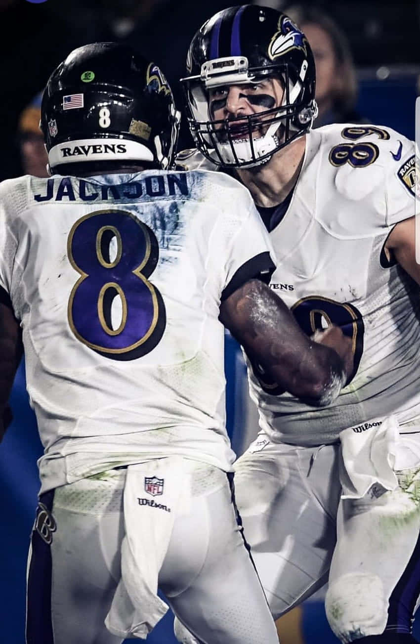 Ravens 桌布 壁紙 — 兩名身穿白色球衣的巴爾的摩烏鴉隊美式足球員在體育場燈光下的夜間比賽中激烈慶祝。