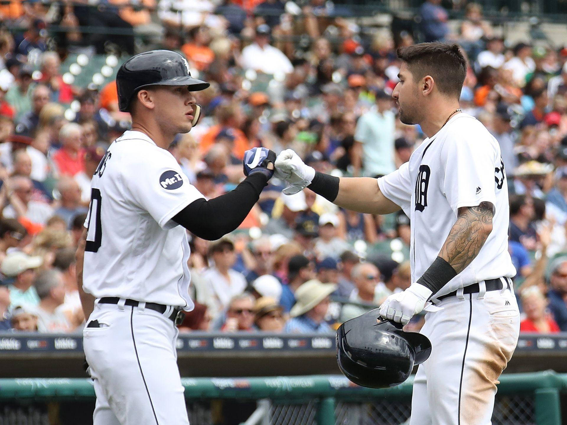 Nick Castellanos 桌布 壁紙 — 兩名身穿白色球衣的棒球運動員在陽光明媚的球場上互相碰拳，背景是模糊的人群。