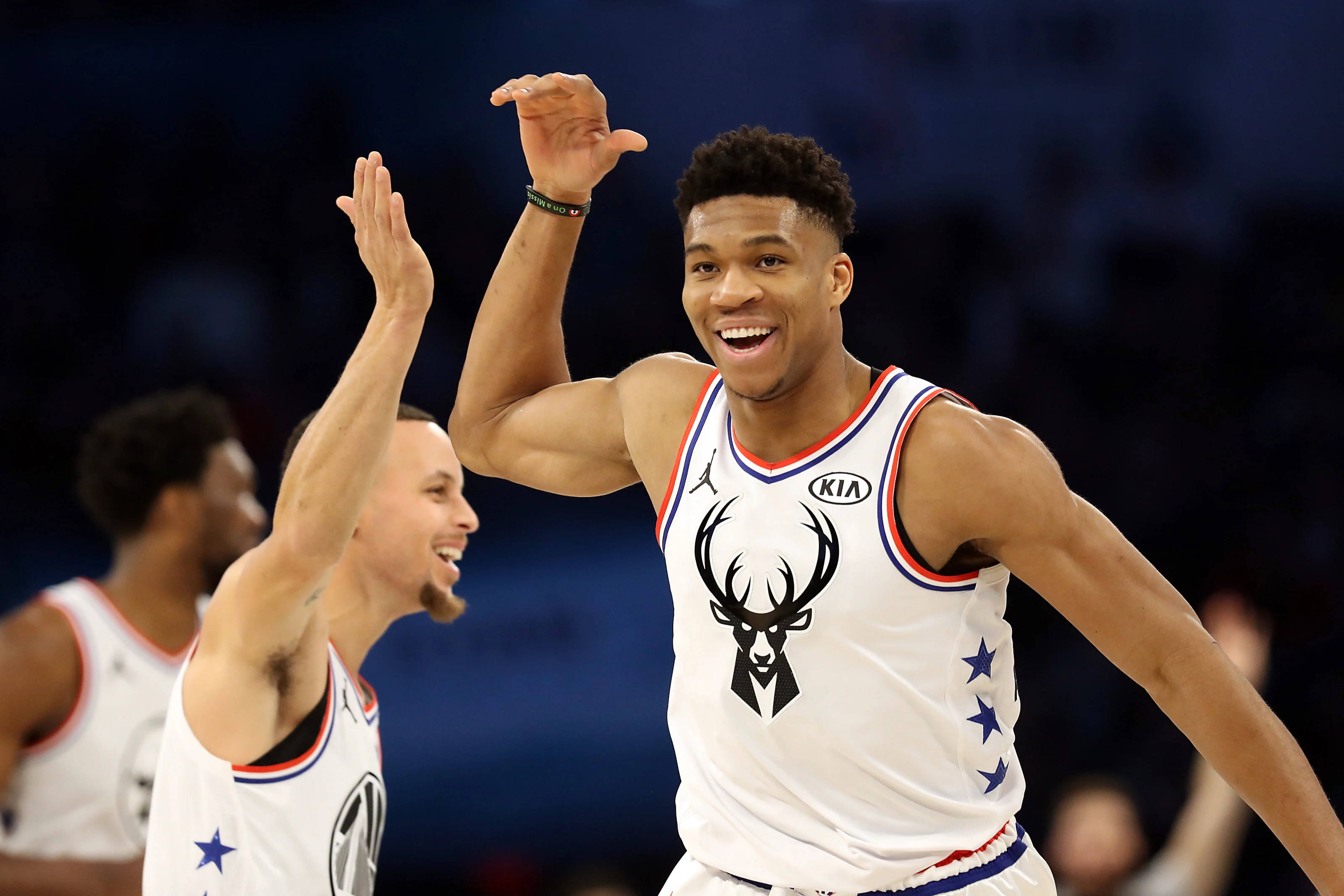 Giannis 桌布 壁紙 — 兩名身穿白色球衣的籃球運動員在比賽期間於場館燈光下擊掌慶祝。