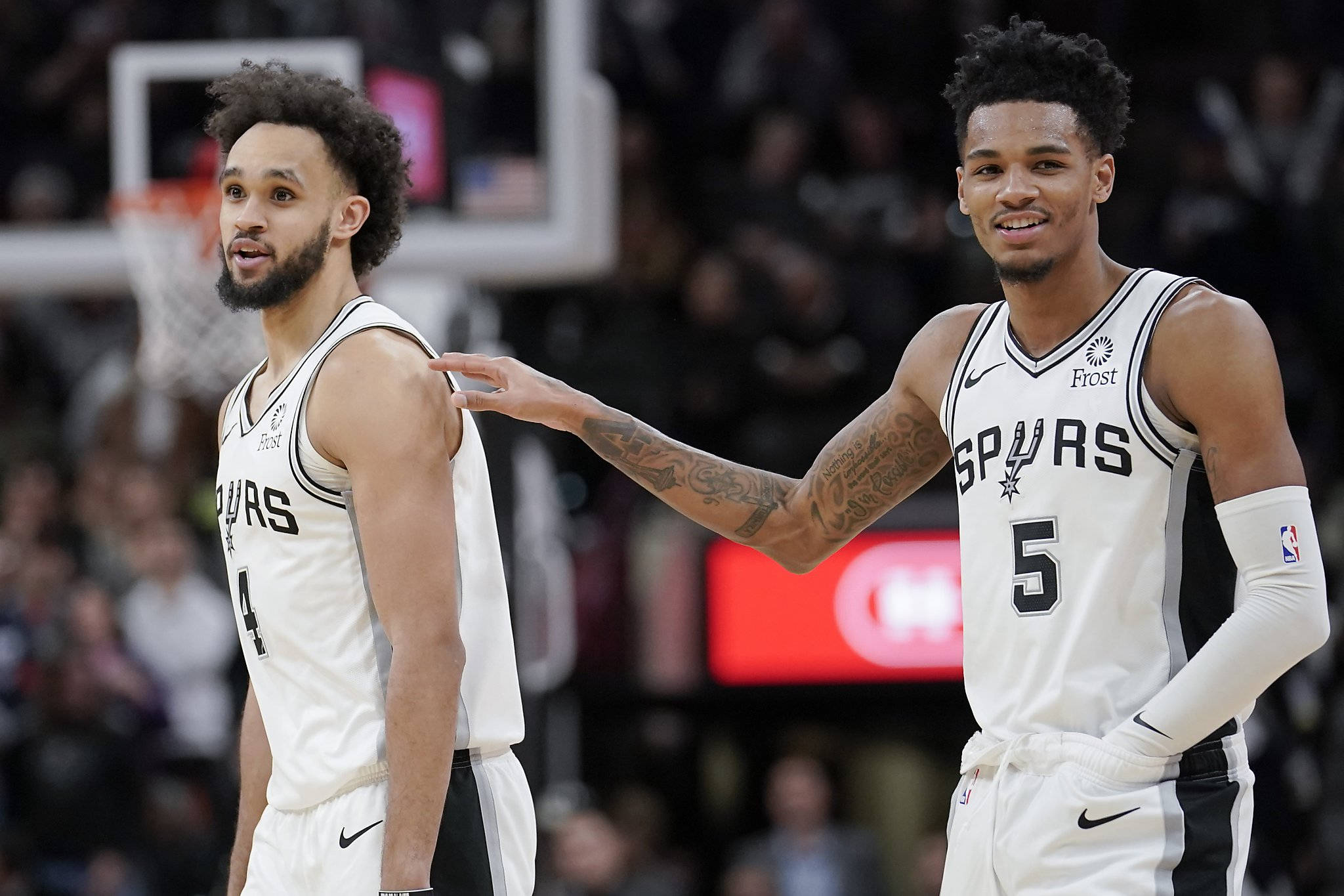 Dejounte Murray 桌布 壁紙 — 兩名身穿白色球衣的聖安東尼奧馬刺籃球運動員在球場上分享一個時刻，其中一人輕拍另一人的肩膀。