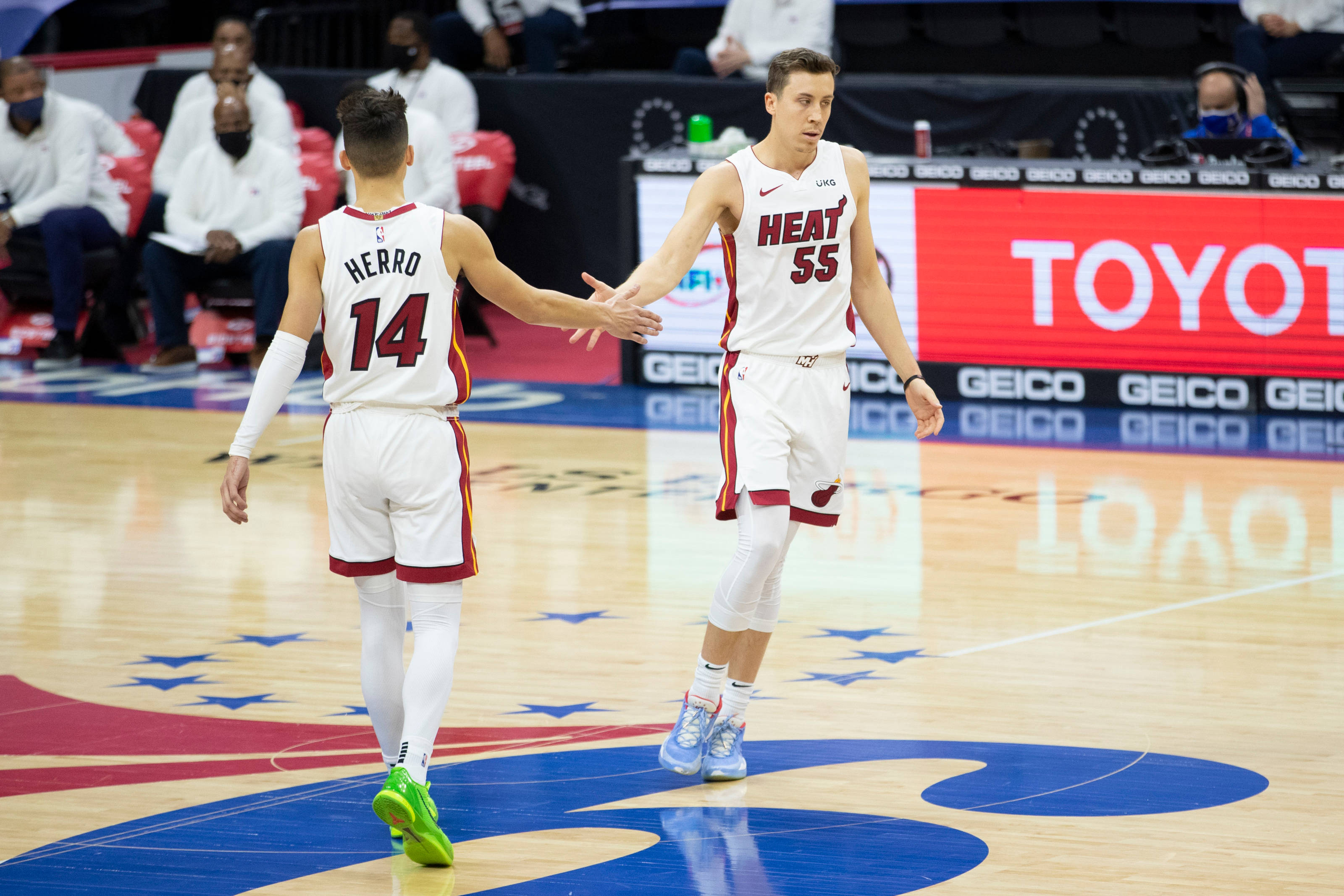 duncan robinson 桌布 壁紙 — 兩名身穿白色球衣的邁阿密熱火籃球運動員在拋光木地板上握手，場地可見球隊標誌和贊助商廣告。