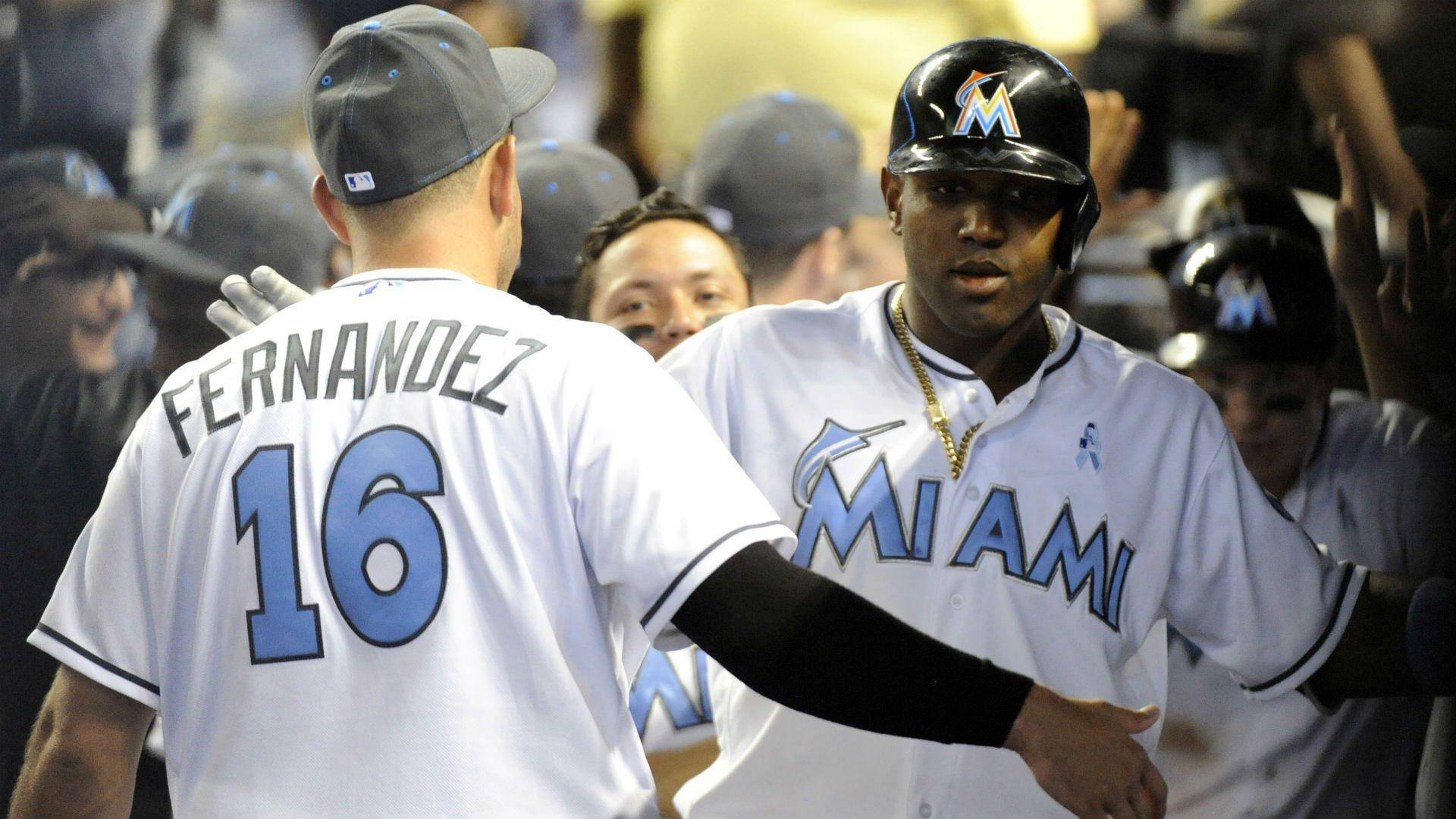 MLB 桌布 壁紙 — 兩名身穿白色球衣的邁阿密馬林魚棒球選手在擁擠的球員休息區內，在球場燈光下擊掌。