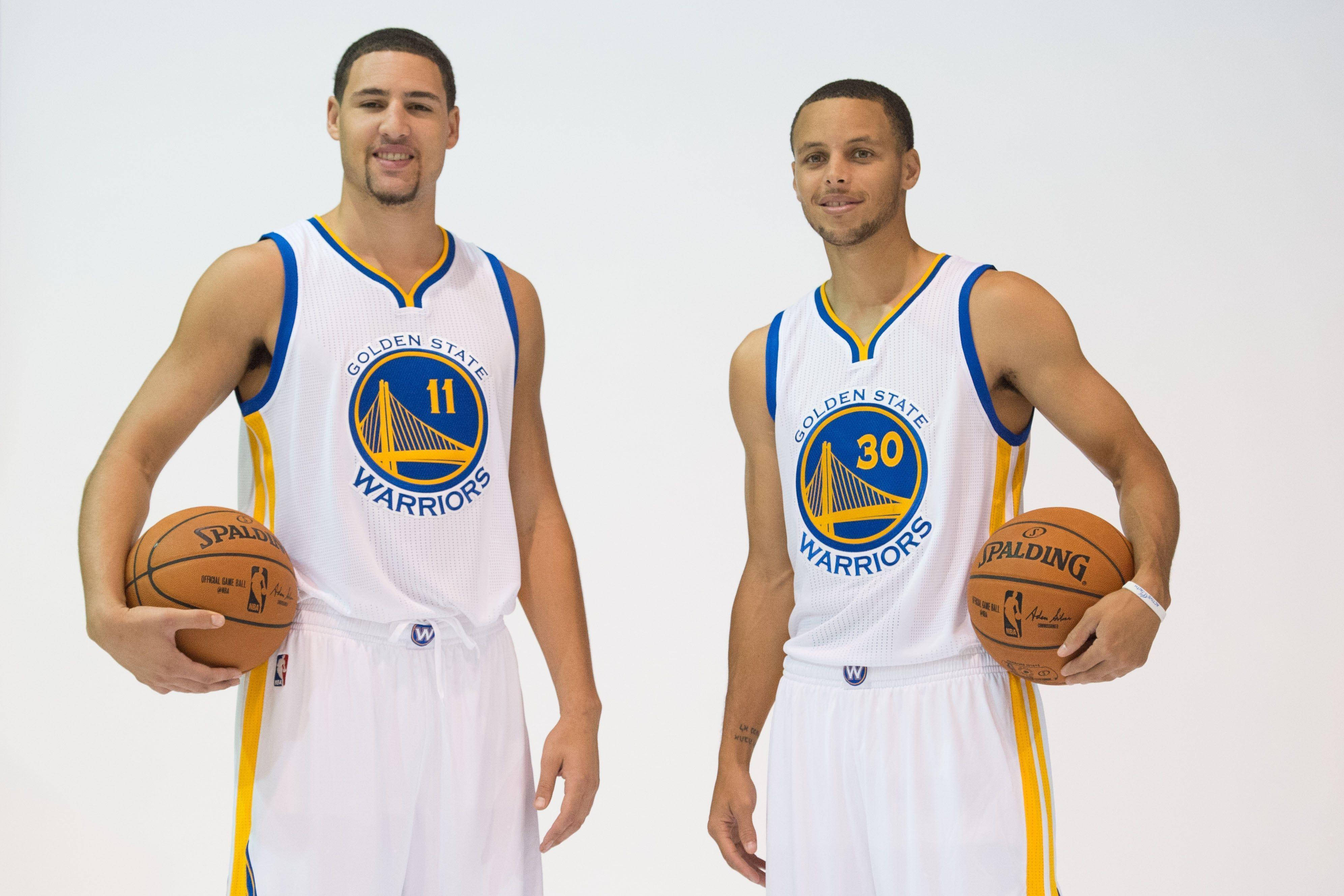 Thompson 桌布 壁紙 — 兩名身穿白色球衣的金州勇士籃球運動員，在純白色背景前手持Spalding籃球。