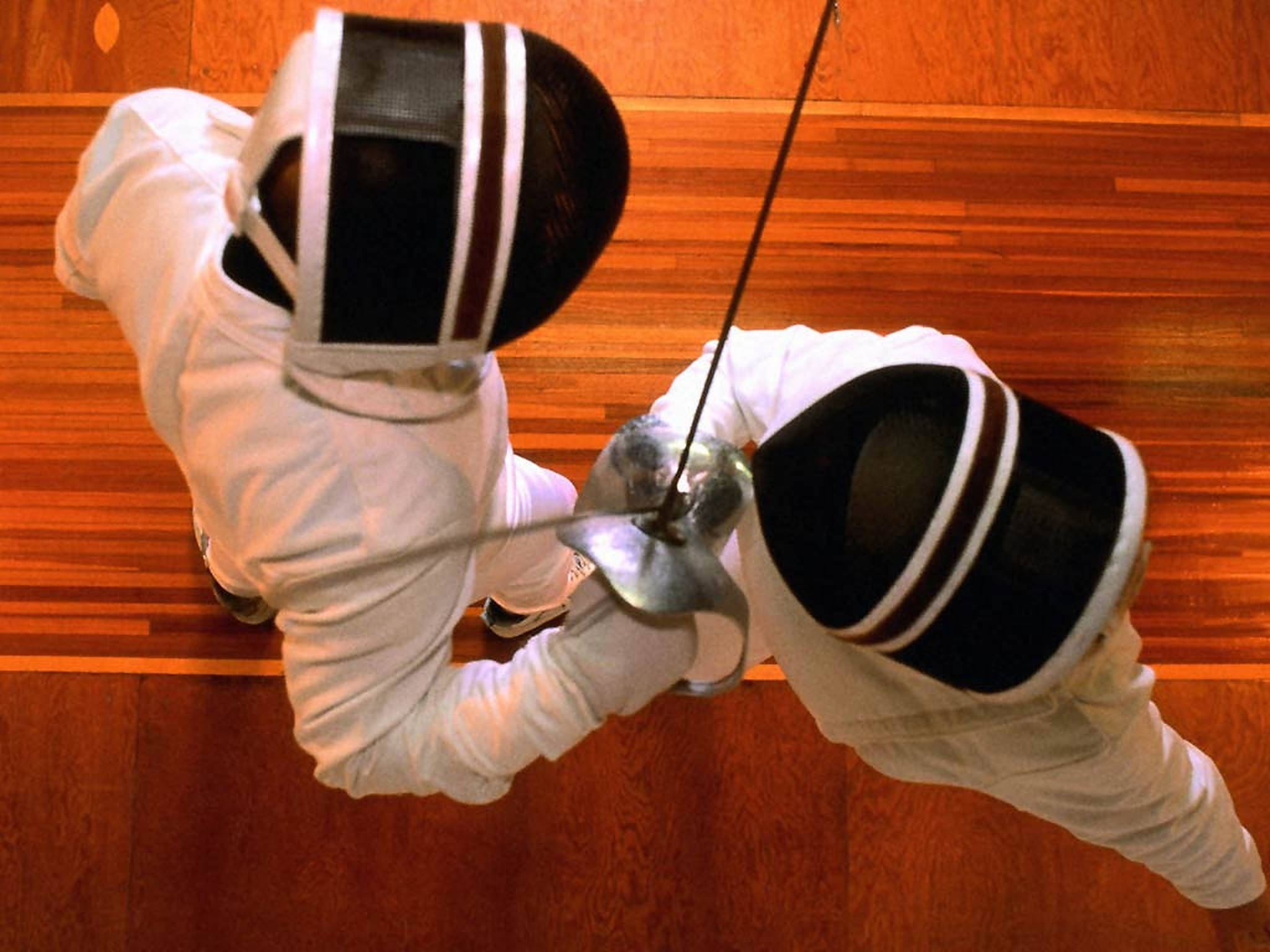 Fencing 桌布 壁紙 — 兩名身穿白色裝備和黑色面罩的劍擊手在木地板上從俯視角度交劍。