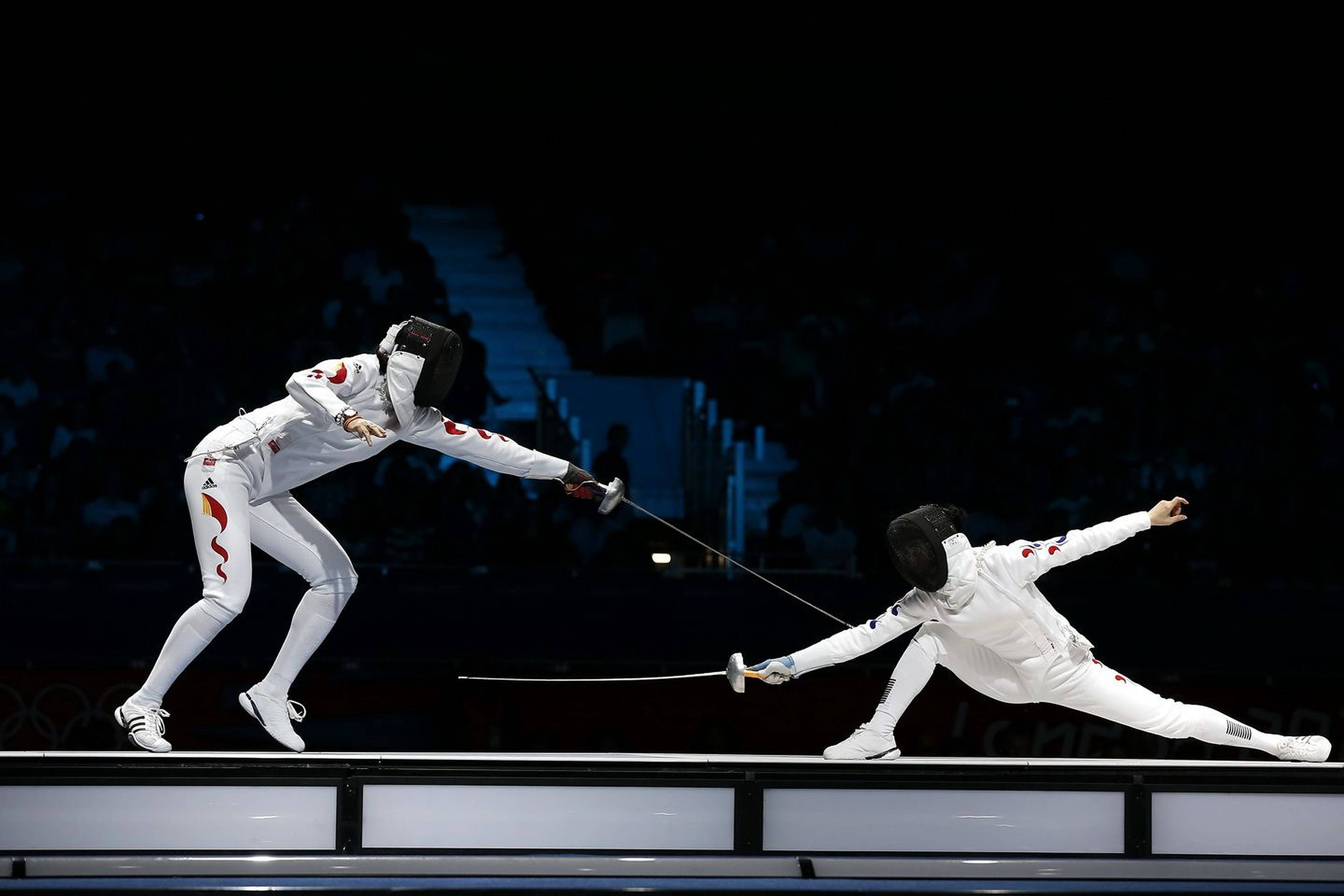 Fencing 桌布 壁紙 — 兩名身穿白色裝備的劍擊運動員在明亮的場館燈光下，於一場戲劇性的奧運比賽中交鋒。