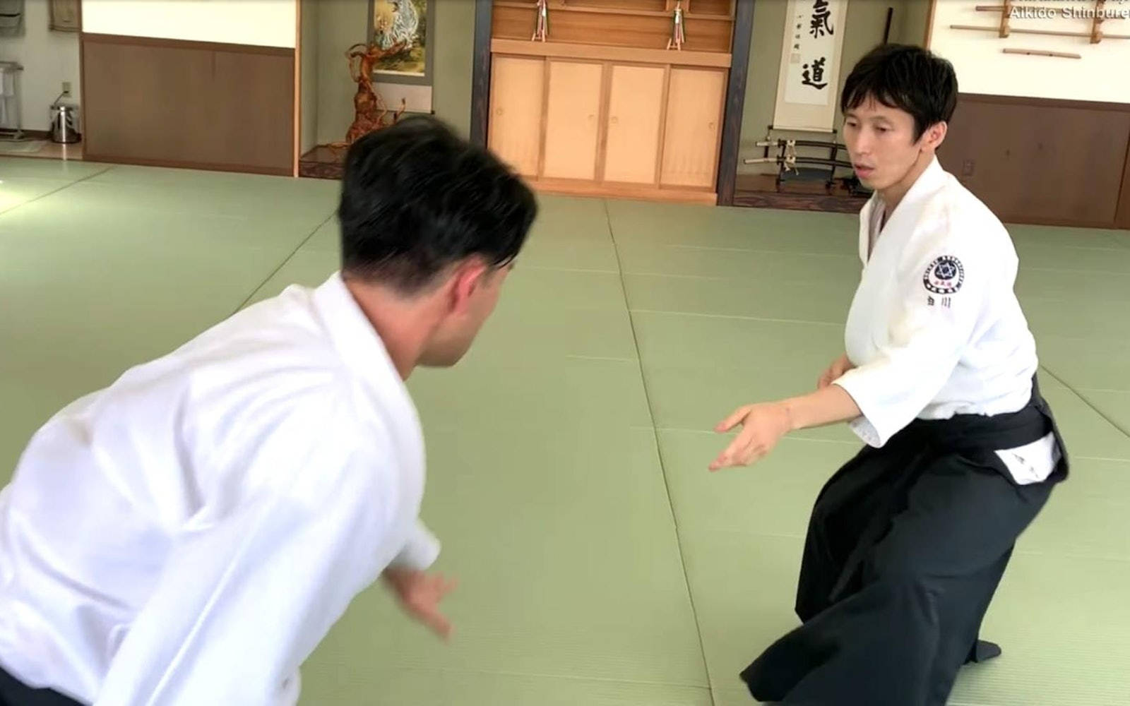 martial arts 桌布 壁紙 — 兩名身穿白色道服的男子在傳統道場的綠色榻榻米上練習合氣道，道場有木牆和書法。