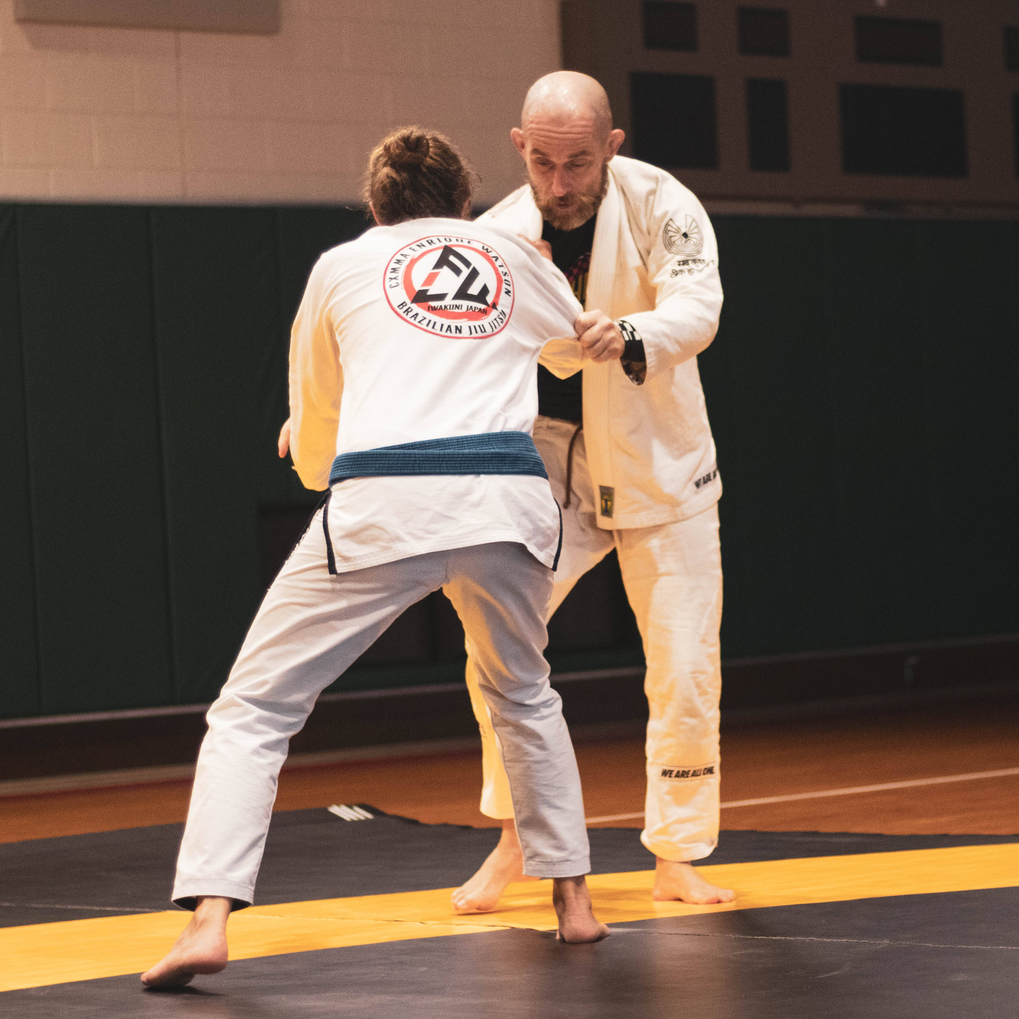 Judo 桌布 壁紙 — 兩名身穿白色道服的運動員在體育館內的黑黃色墊子上激烈纏鬥。