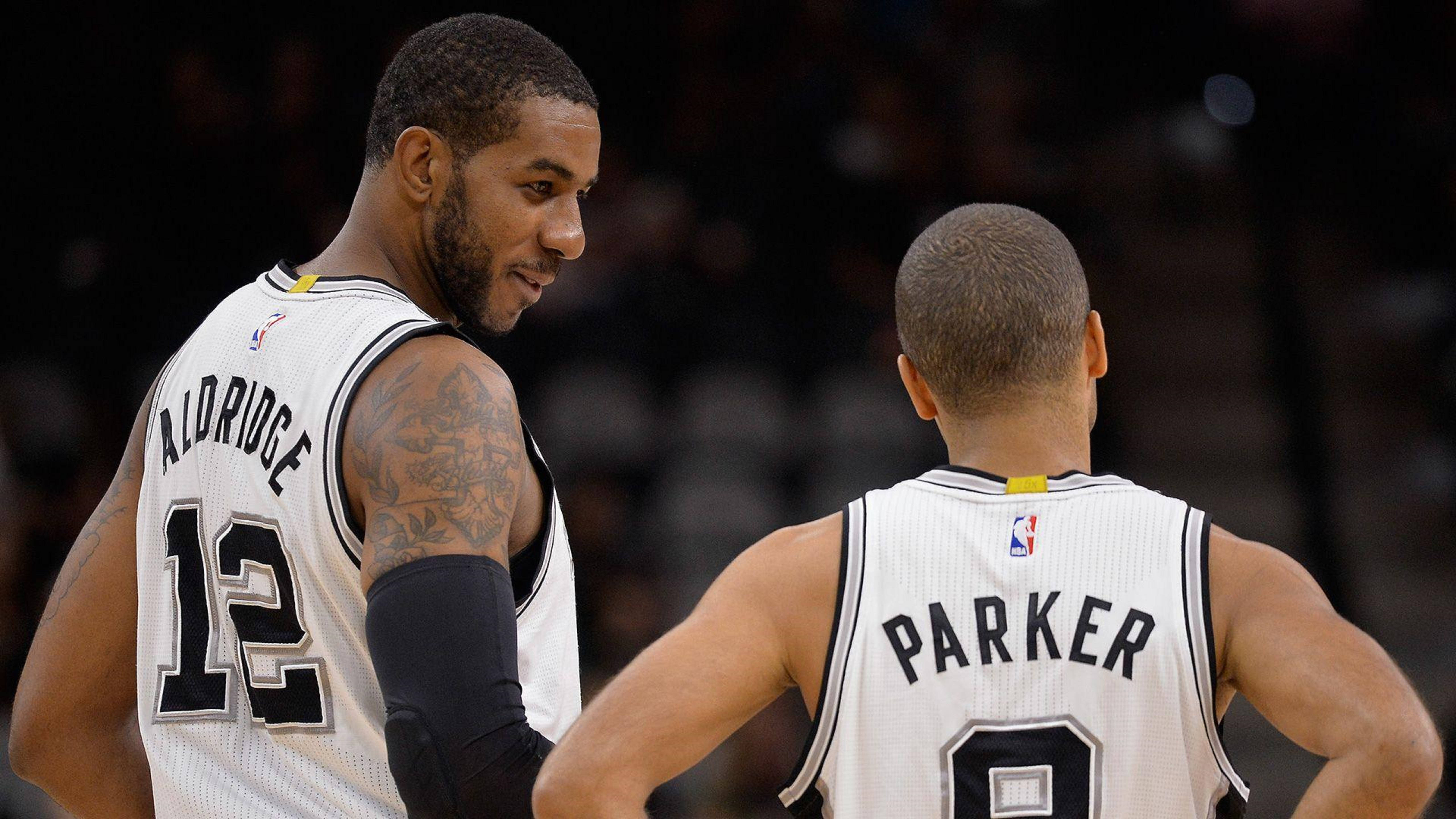 Lamarcus Aldridge 桌布 壁紙 — 兩名身穿白色馬刺隊球衣的籃球運動員在明亮的場館燈光下，於比賽中激烈交談。