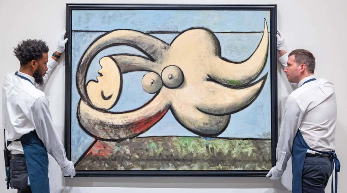 Picasso 桌布 壁紙 — 兩名身穿白襯衫和手套的修復師小心地懸掛一幅大型抽象畫，畫中有一隻超現實的米色生物，有眼睛和彎曲的角，背景是藍天和綠地。
