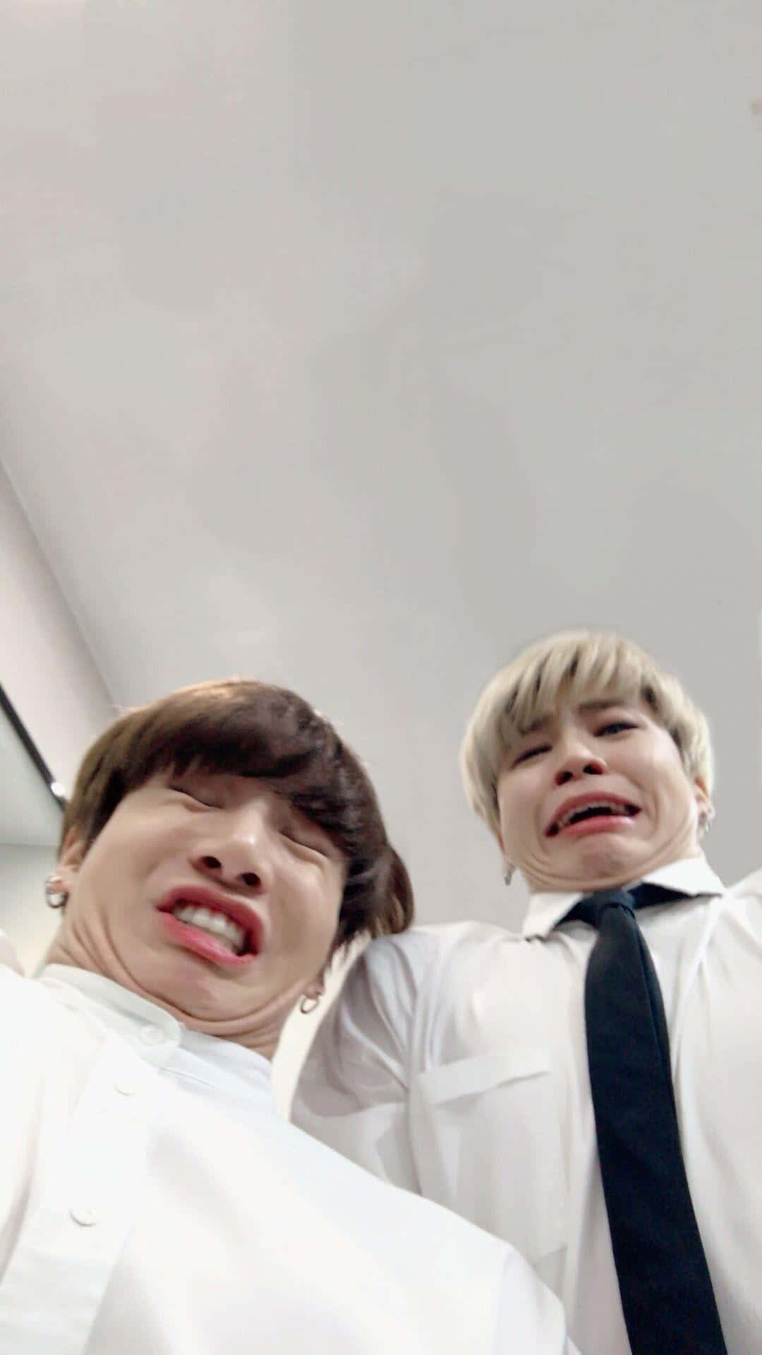 Bts Funny 桌布 壁紙 — 兩名身穿白襯衫的年輕男子在普通天花板背景下為自拍做出誇張的傻臉。