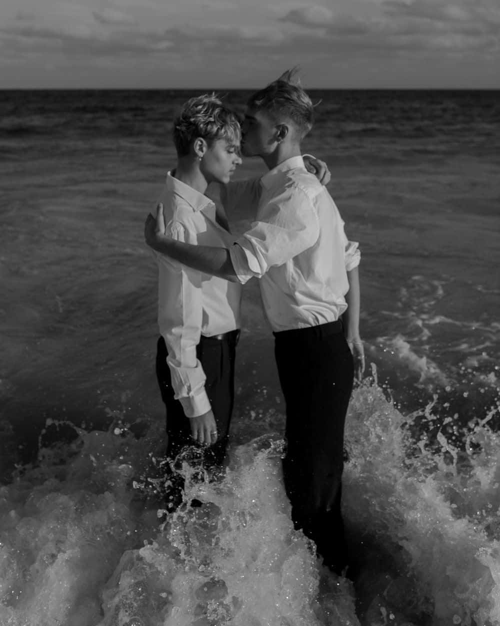 Lovers 桌布 壁紙 — 兩名身穿白襯衫的男子在黃昏的海浪中溫柔相擁，黑白照片。