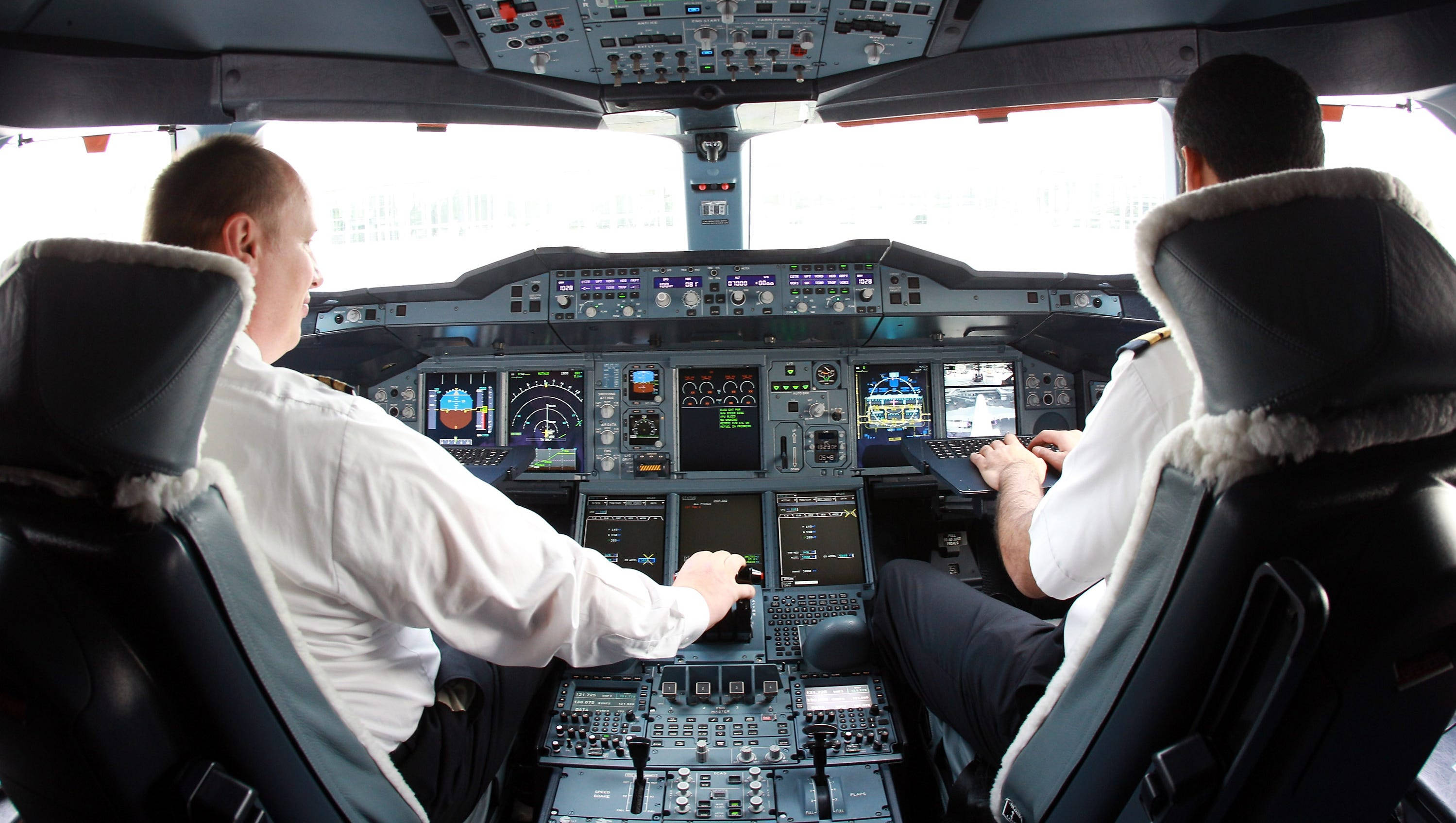 Aviation 桌布 壁紙 — 兩名身穿白襯衫的飛行員坐在現代飛機駕駛艙內，在飛行期間管理控制裝置和螢幕。