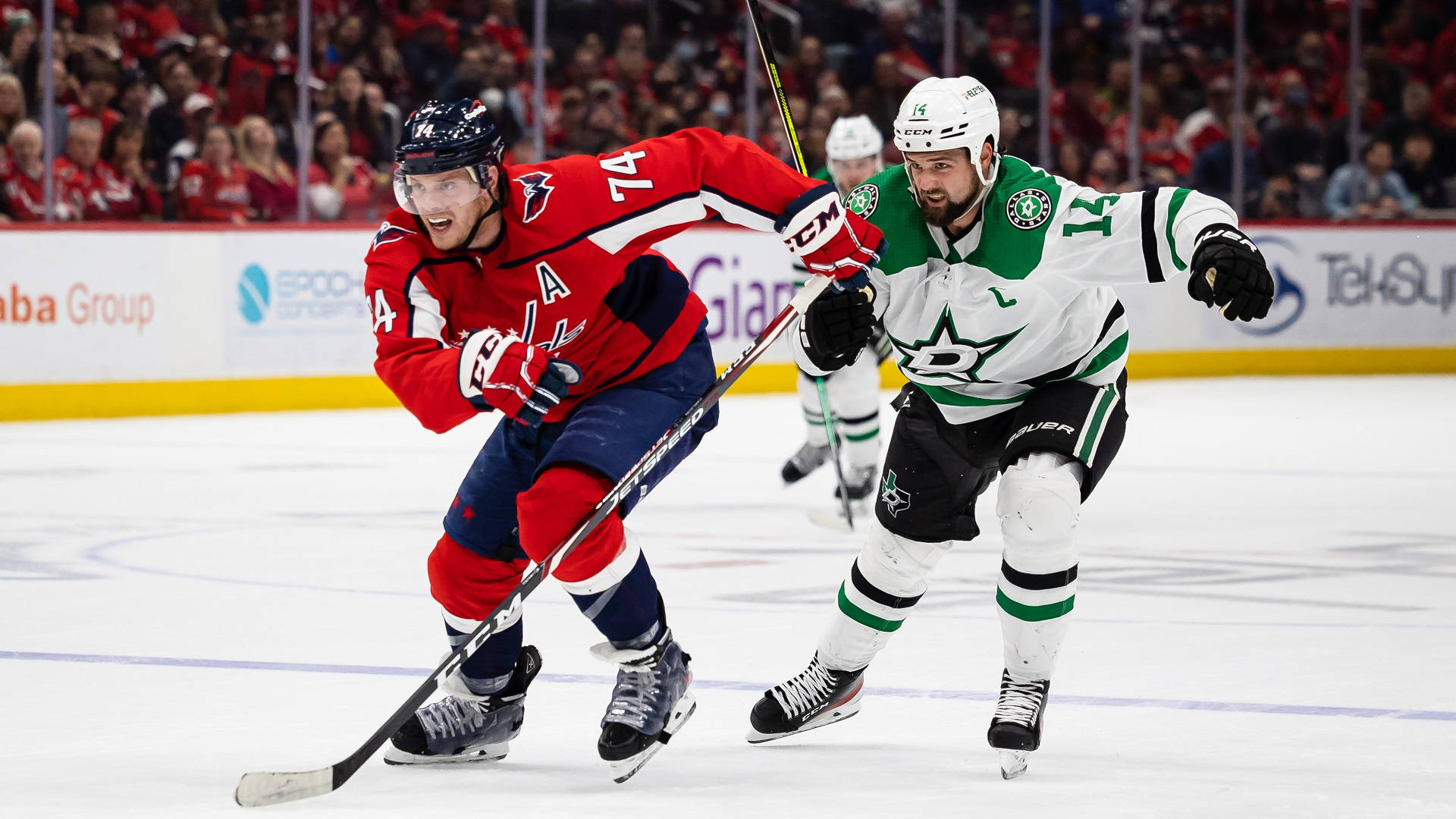 Dallas Stars 桌布 壁紙 — 兩名身穿紅色和綠色球衣的冰球運動員在燈光明亮的冰場上激烈爭奪冰球，背景有球迷。