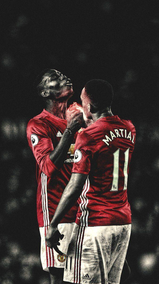 Anthony Martial 桌布 壁紙 — 兩名身穿紅色曼聯球衣的足球員在黑暗模糊的球場背景下深情擁抱。