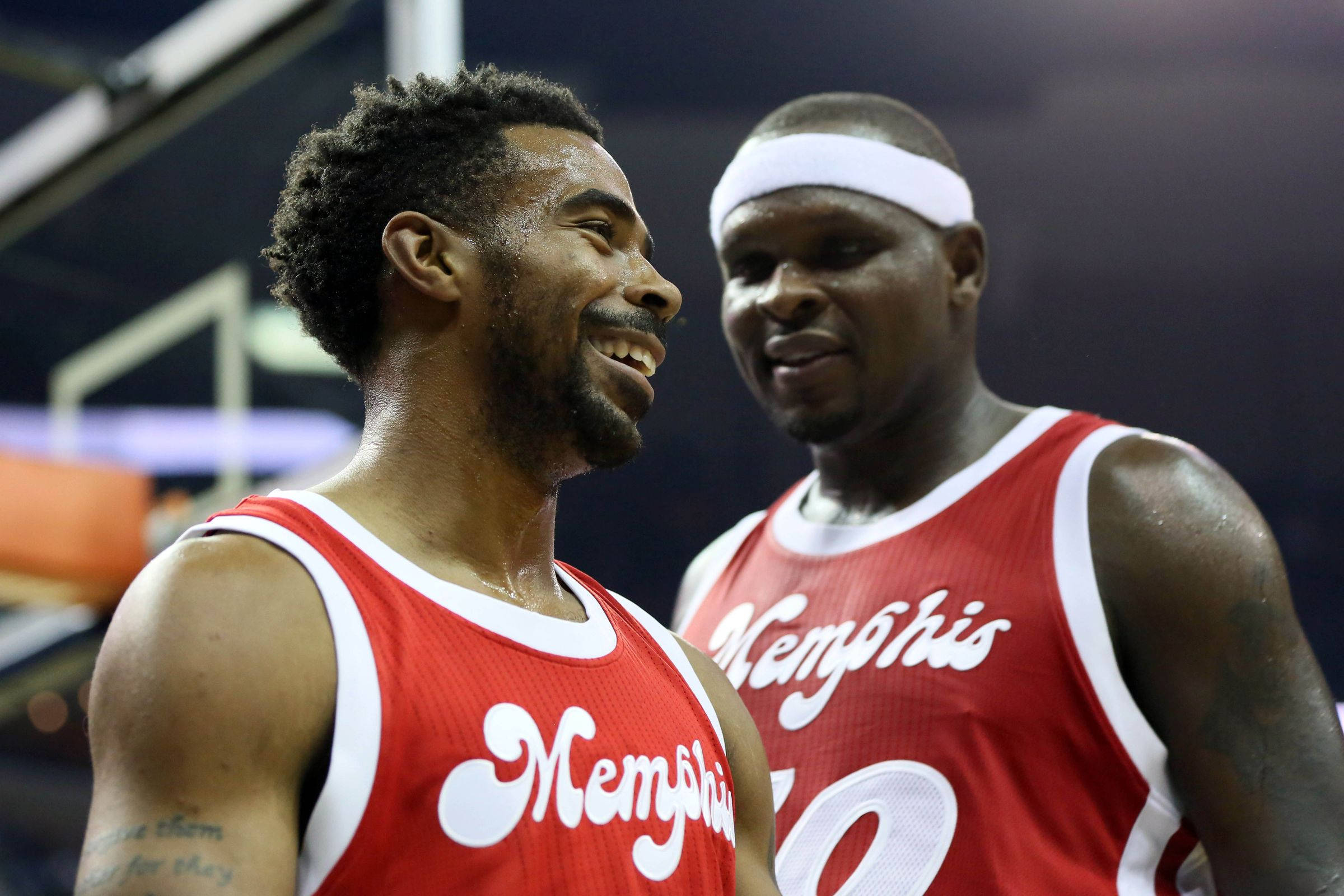 Grizzlies 桌布 壁紙 — 兩名身穿紅色曼菲斯球衣的籃球運動員笑容滿面，在燈光明亮的球場上分享歡樂時刻。