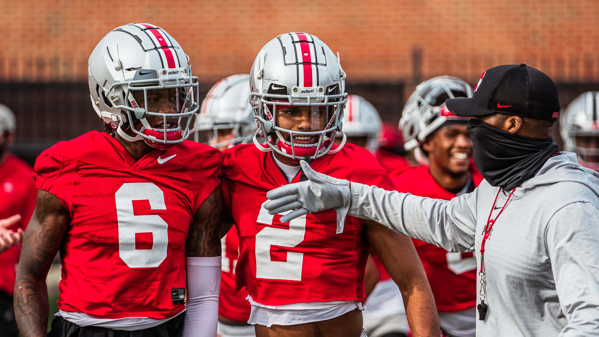 Cool Ohio State 桌布 壁紙 — 兩名身穿紅色球衣、號碼6和2的足球員微笑著站在教練旁邊，教練在訓練期間做手勢。