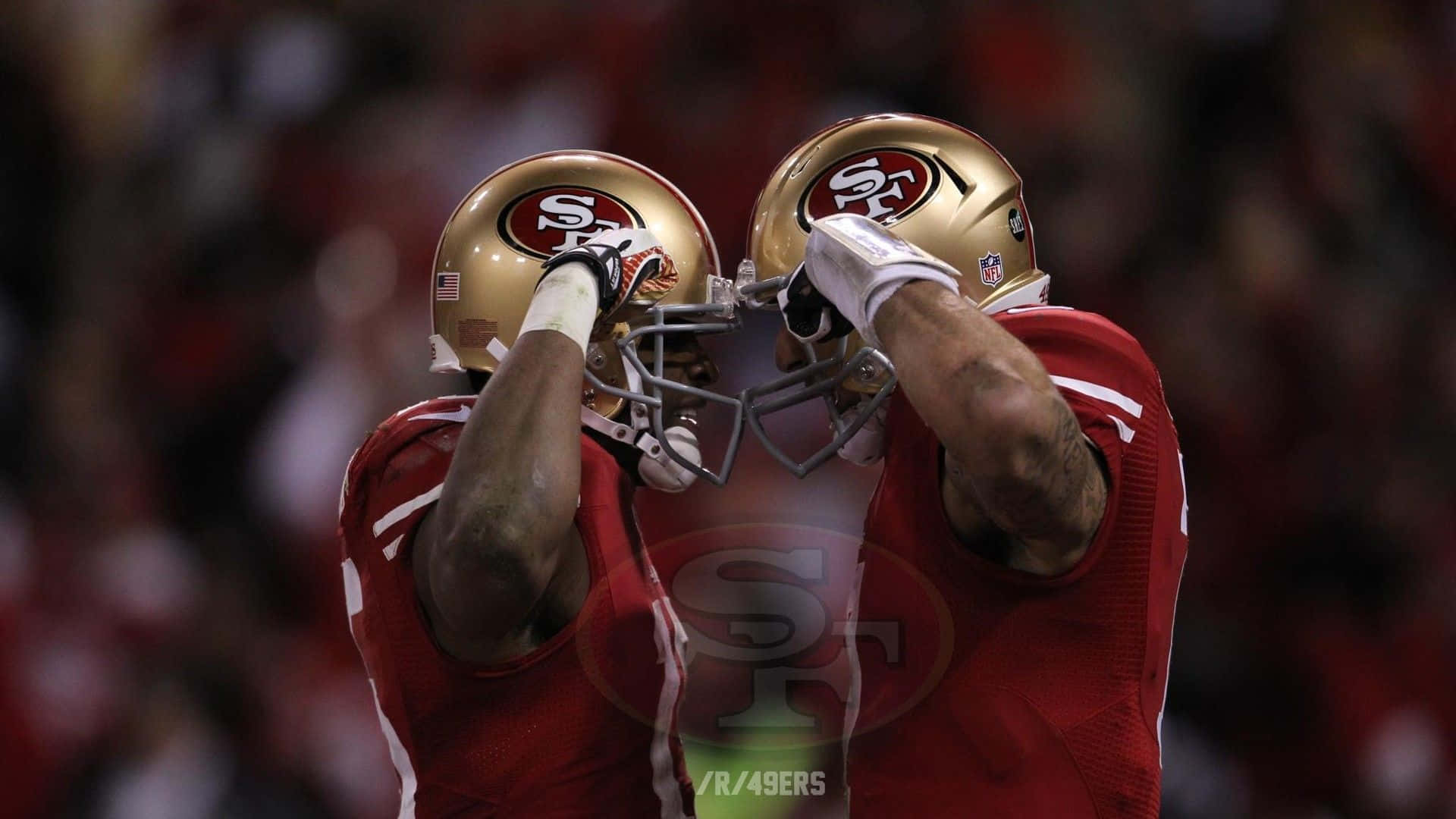 49ers 桌布 壁紙 — 兩名身穿紅色球衣和金色頭盔的舊金山四九人美式足球員在場上以頭盔相觸慶祝。