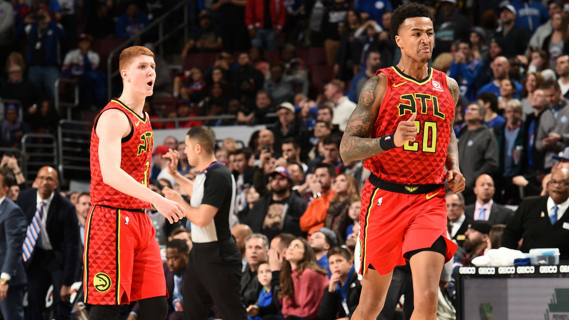 John Collins 桌布 壁紙 — 兩名身穿紅色球衣的亞特蘭大老鷹隊籃球運動員在比賽中激烈反應，背景是擠滿的人群。