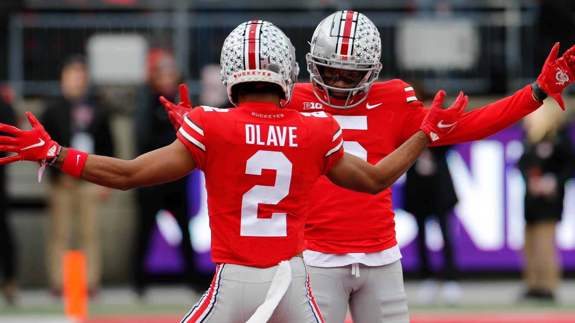 Cool Ohio State 桌布 壁紙 — 兩名身穿紅色球衣的俄亥俄州立大學美式足球員在球場上張開雙臂慶祝。