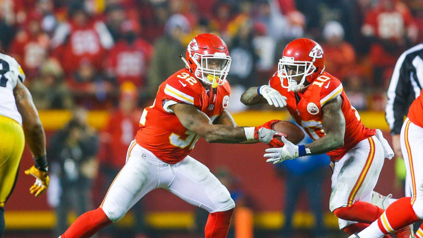 Tyreek Hill 桌布 壁紙 — 兩名身穿紅色球衣的堪薩斯城酋長隊球員在夜間足球比賽中碰撞，其中一人擒抱持球者。