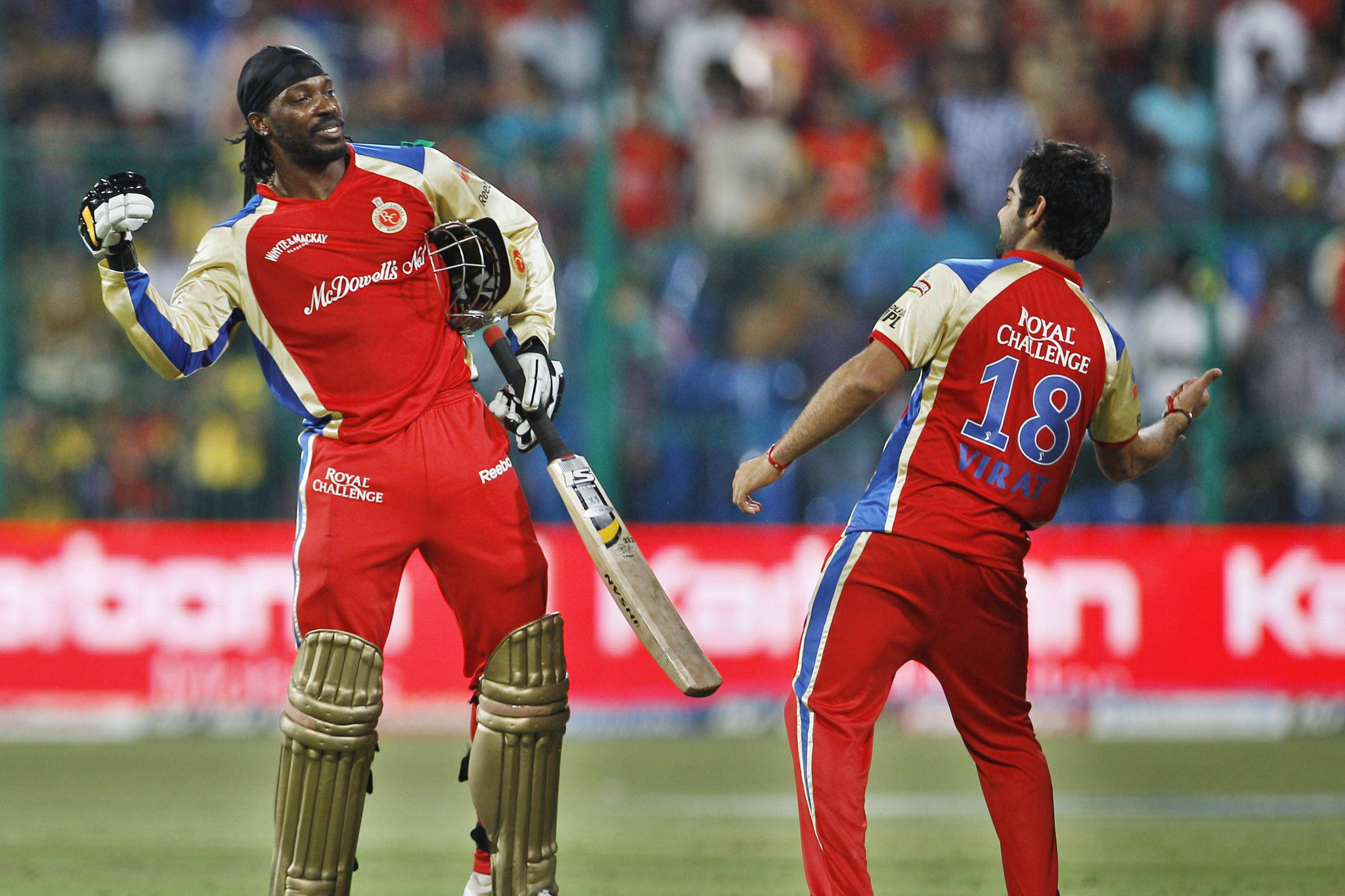 royal challengers bangalore 桌布 壁紙 — 兩名身穿紅色球衣的板球運動員在燈火通明的球場上慶祝，背景有歡呼的球迷。