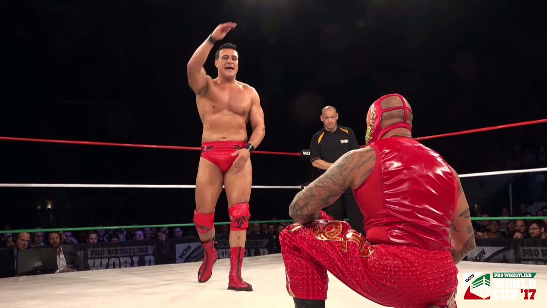 WWE 桌布 壁紙 — 兩名身穿紅色裝備的摔角手在燈光明亮的擂台上對峙，裁判和觀眾專注地觀看。