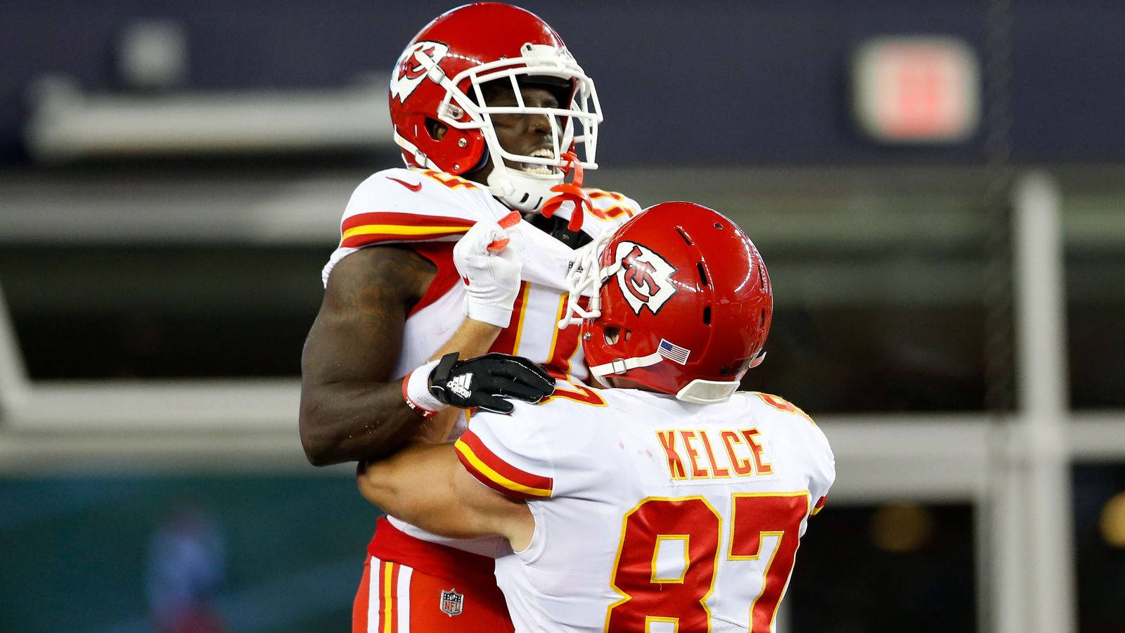 Tyreek Hill 桌布 壁紙 — 兩名身穿紅色頭盔和白色球衣的堪薩斯城酋長隊美式足球員在夜間比賽中在場上緊緊擁抱。